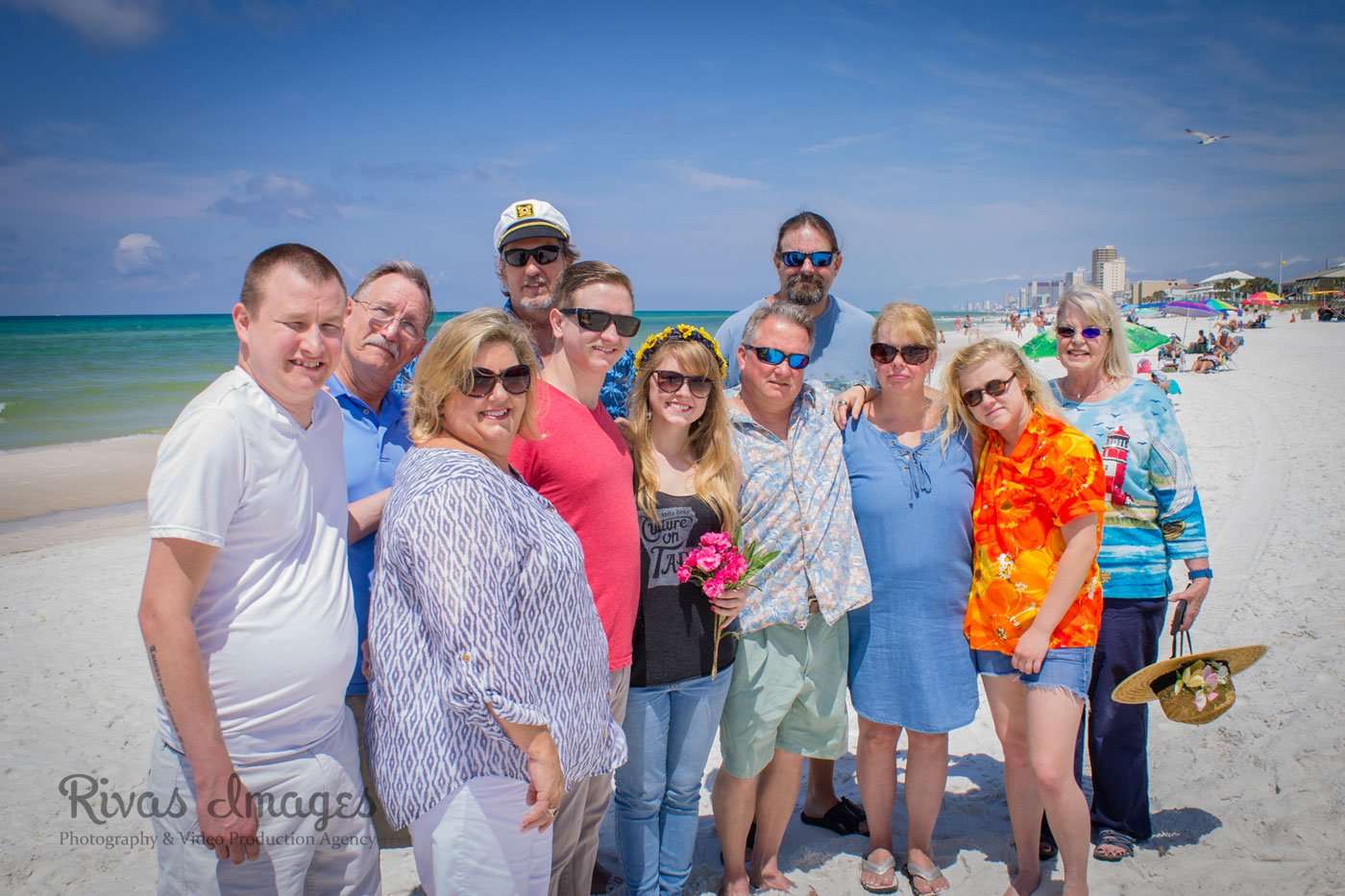 Group of smiling family and friends in sunglasses and colorful summer clothes posing together on a sunny beach
