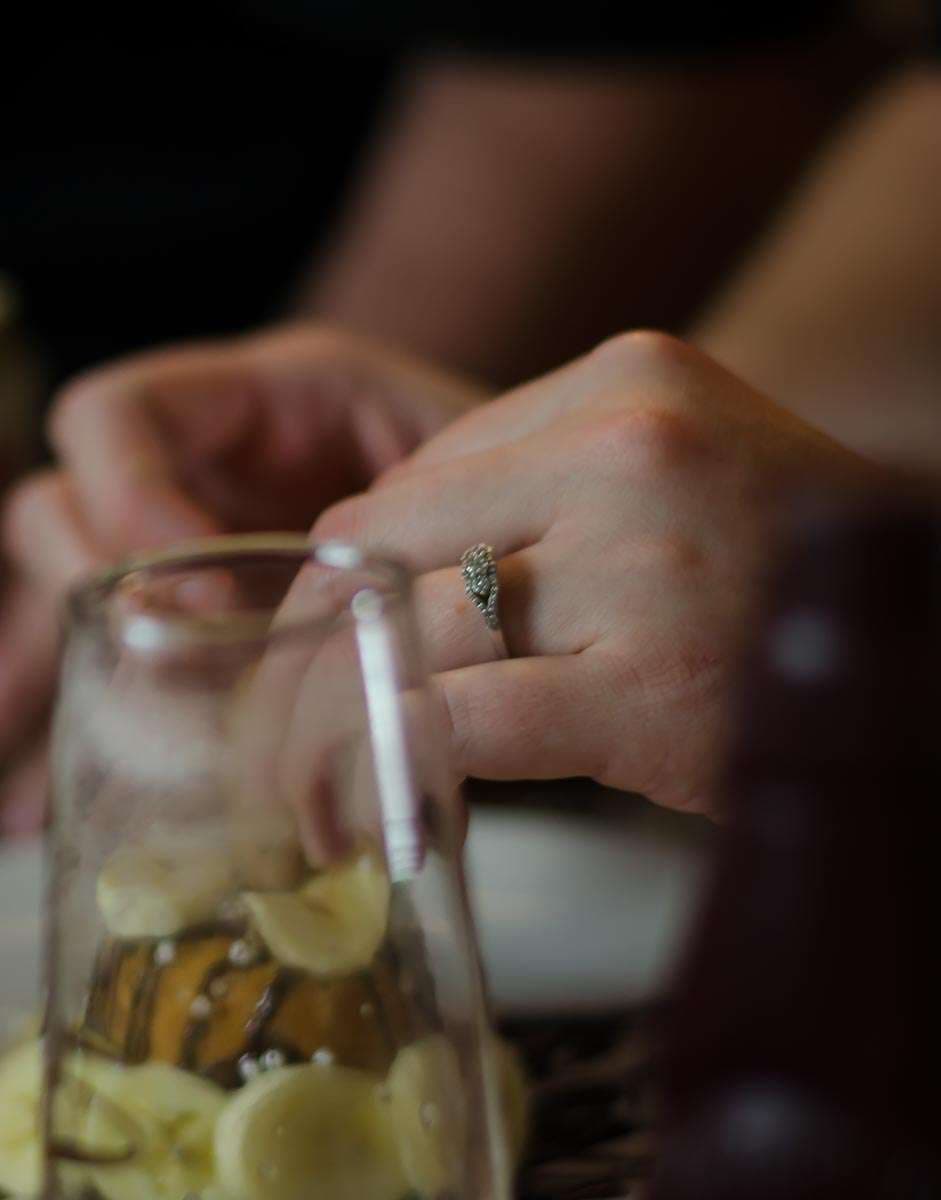 Close-up of a hand wearing a diamond engagement ring resting on a glass jar filled with sliced garlic
