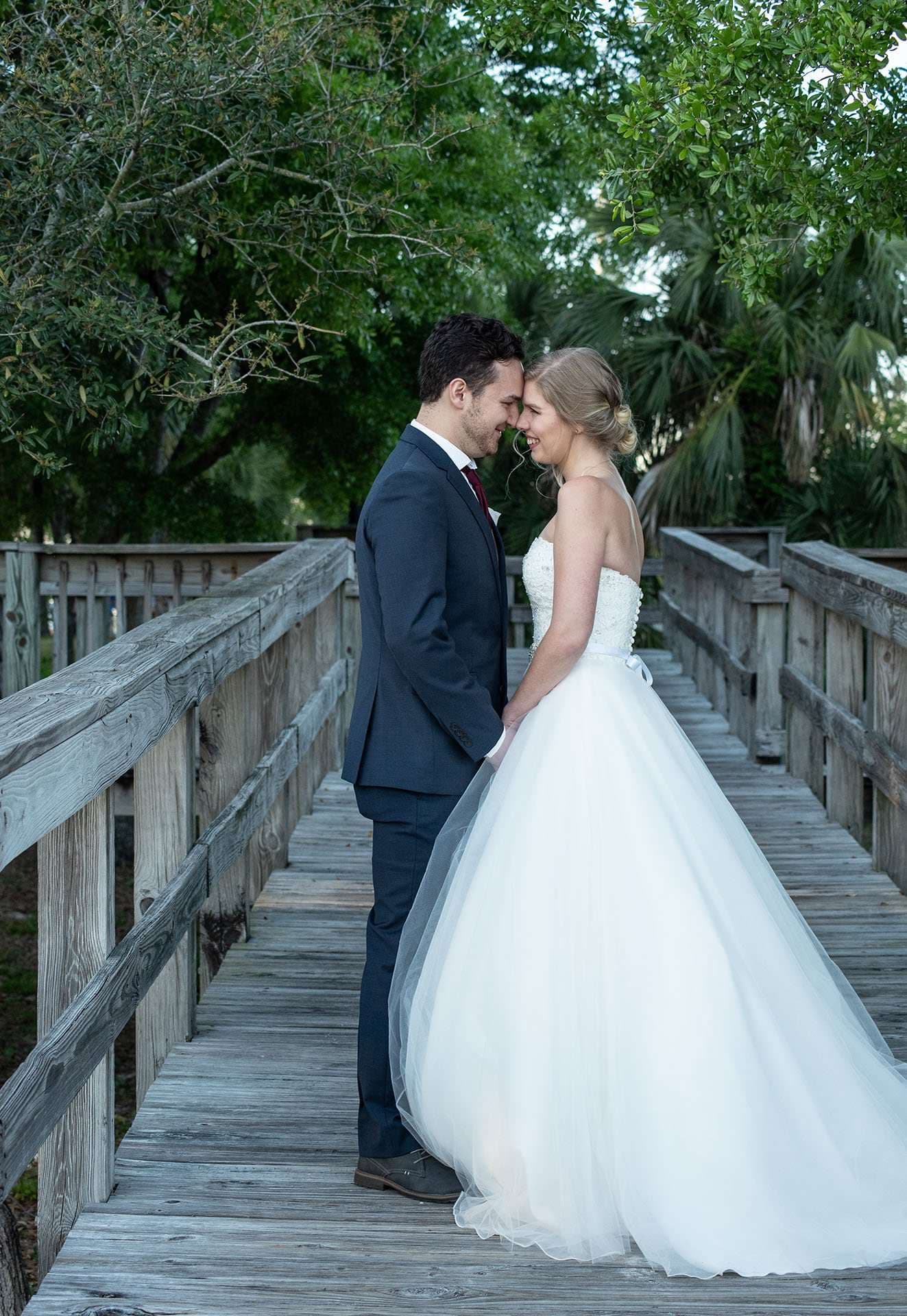 Couple standing forehead to forehead on a weathered wooden boardwalk, bride in a strapless white tulle ball gown