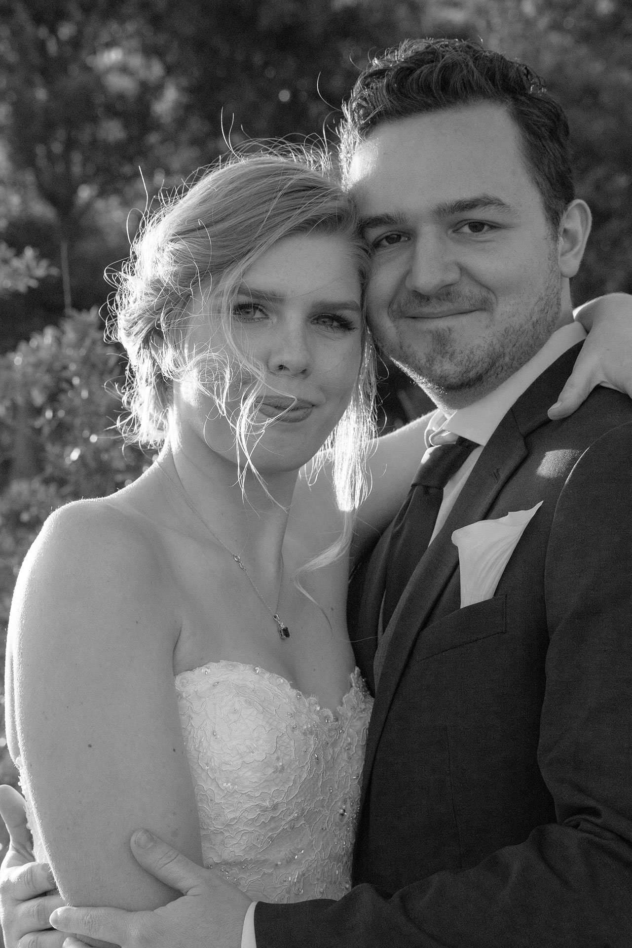 Black-and-white portrait of a couple embracing, her hair blowing in the breeze, he in a suit with pocket square
