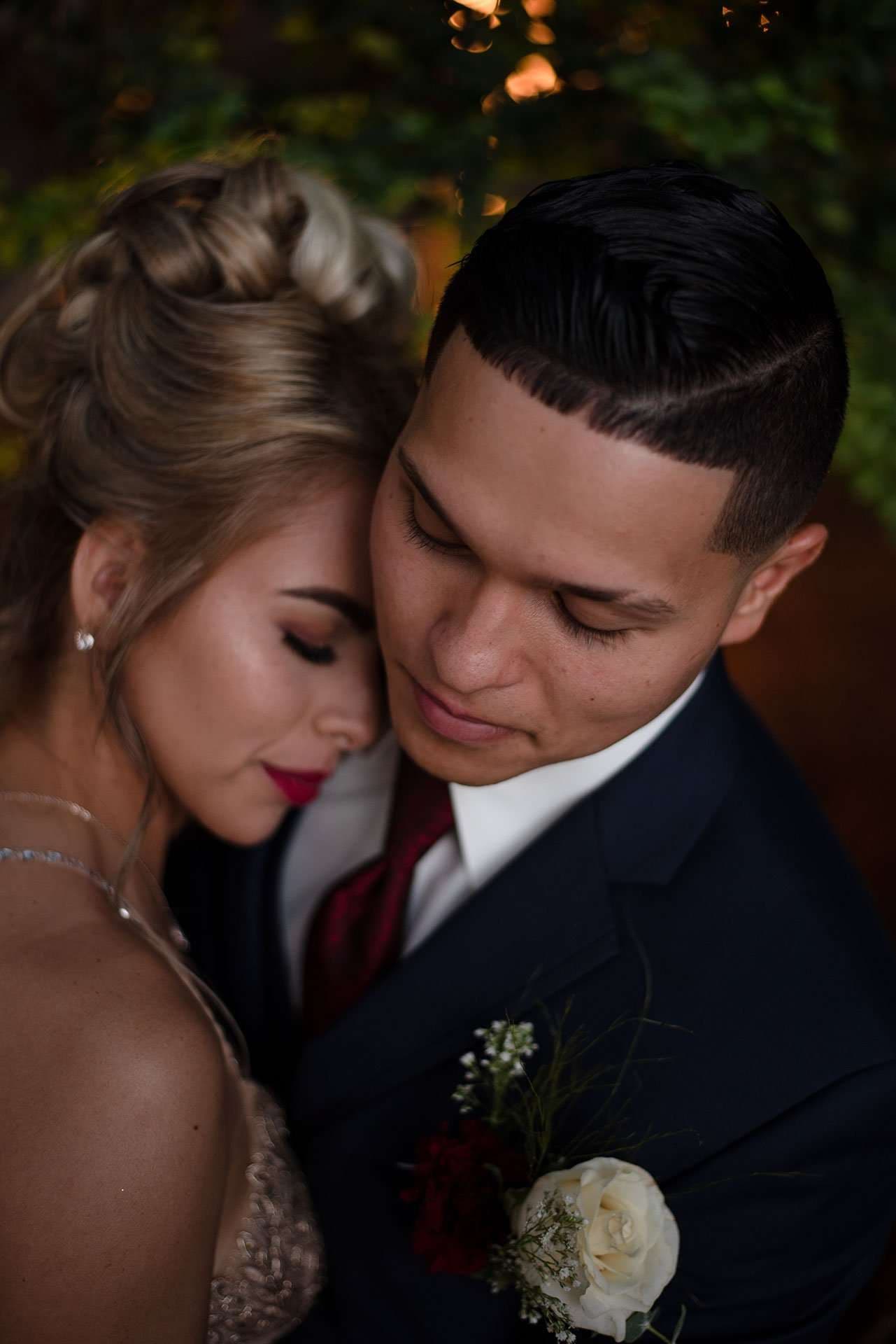 Couple embracing closely, woman with eyes closed and red lipstick, man in navy suit with rose boutonnière