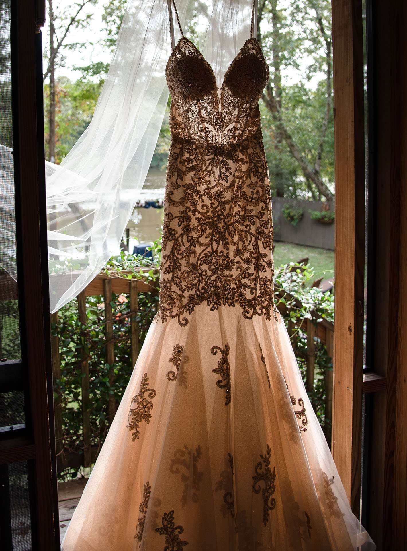 Lace-appliqué wedding gown with a long veil hanging in an open doorway overlooking a wooded deck