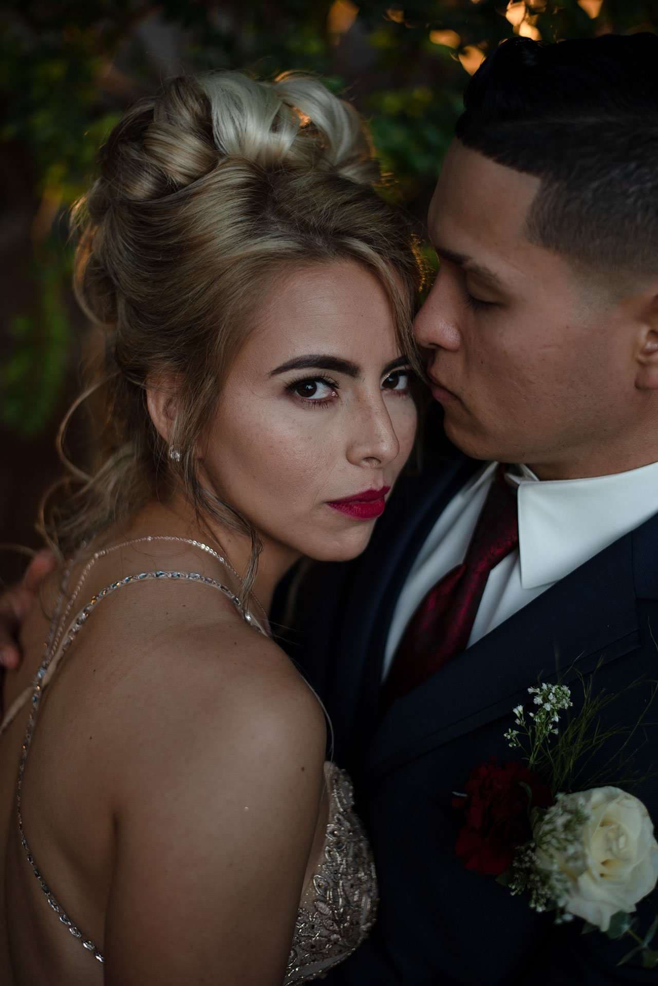 Woman in a beaded gown with red lipstick looks at the camera while a man in a navy suit leans in close