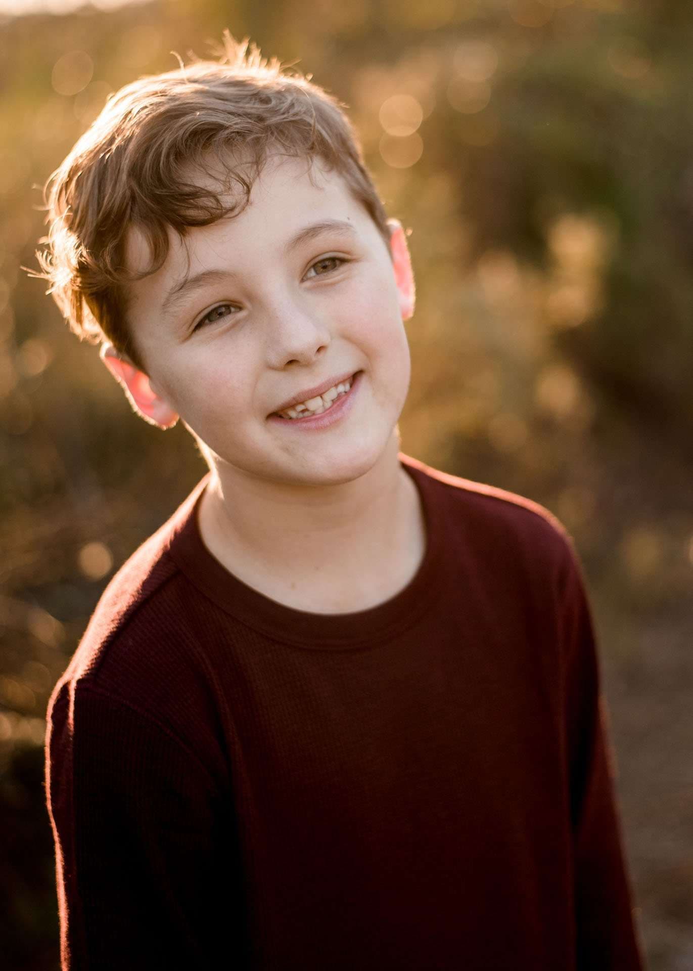 Smiling boy in a maroon sweater tilting his head in warm golden light at the Panama City Beach Conservation Park