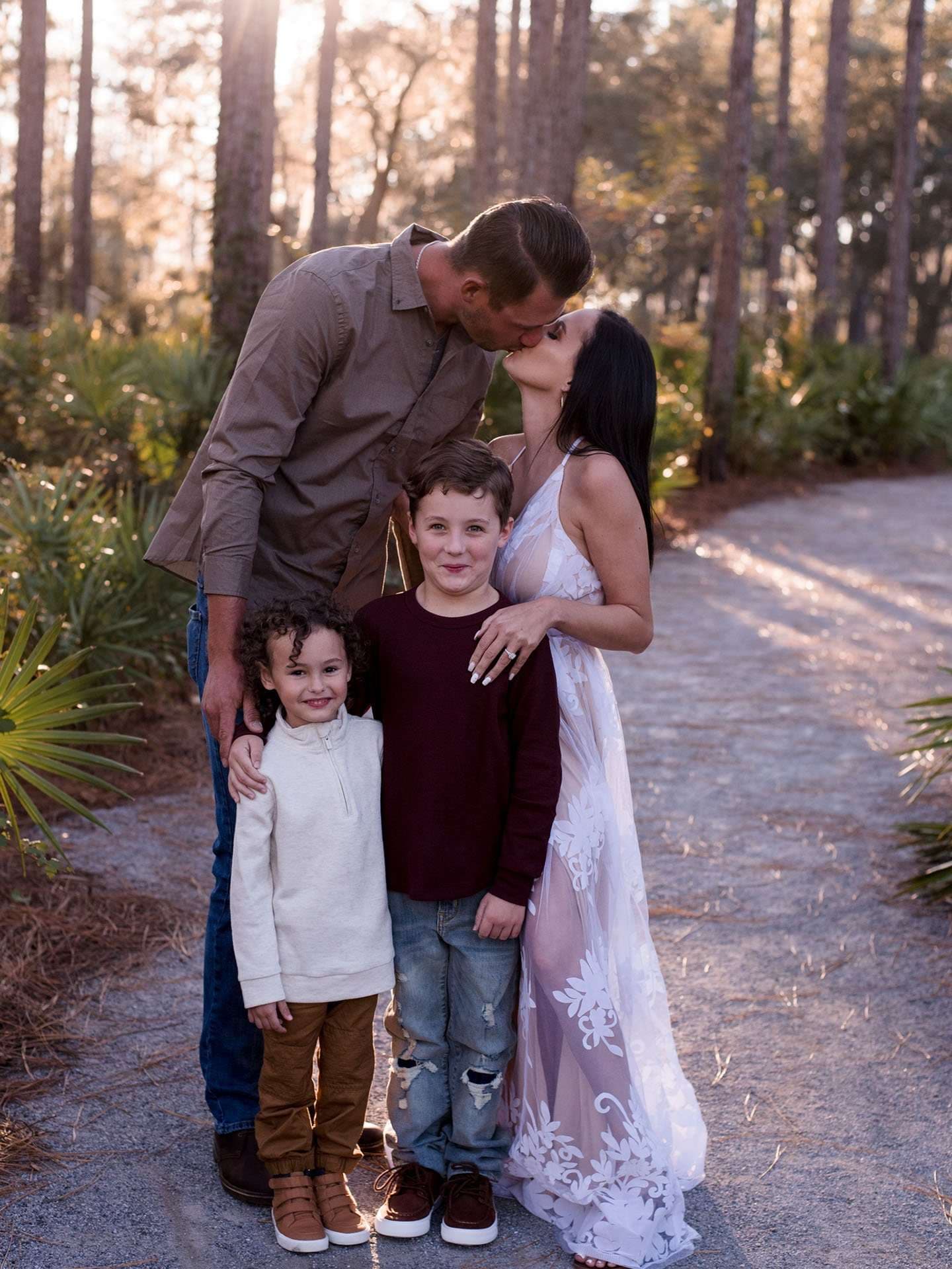 Couple kissing on a wooded path at Panama City Beach Conservation Park, two young boys smiling in front of them