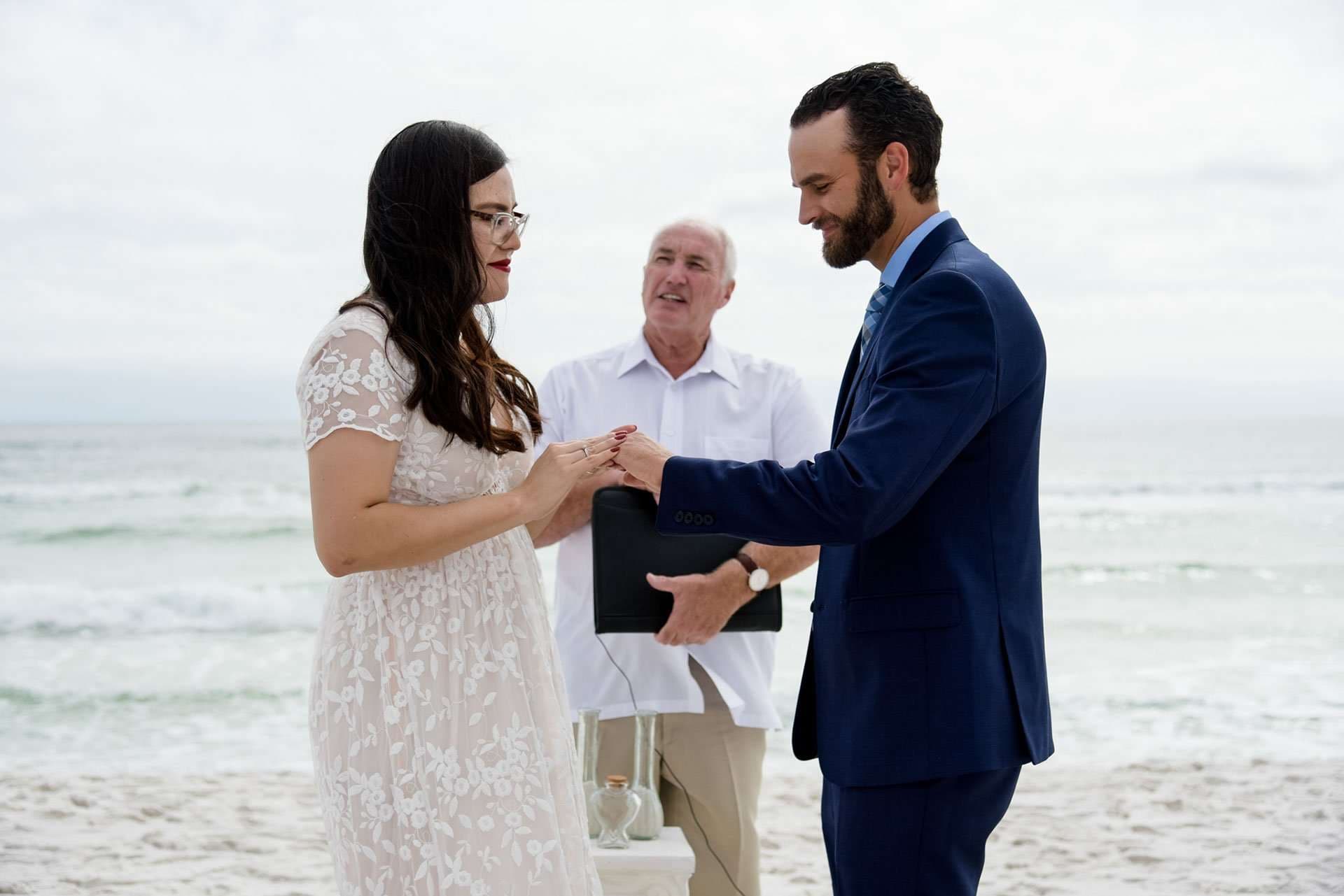 Couple exchanging rings on the beach as an officiant in a white shirt looks on, Okaloosa Island
