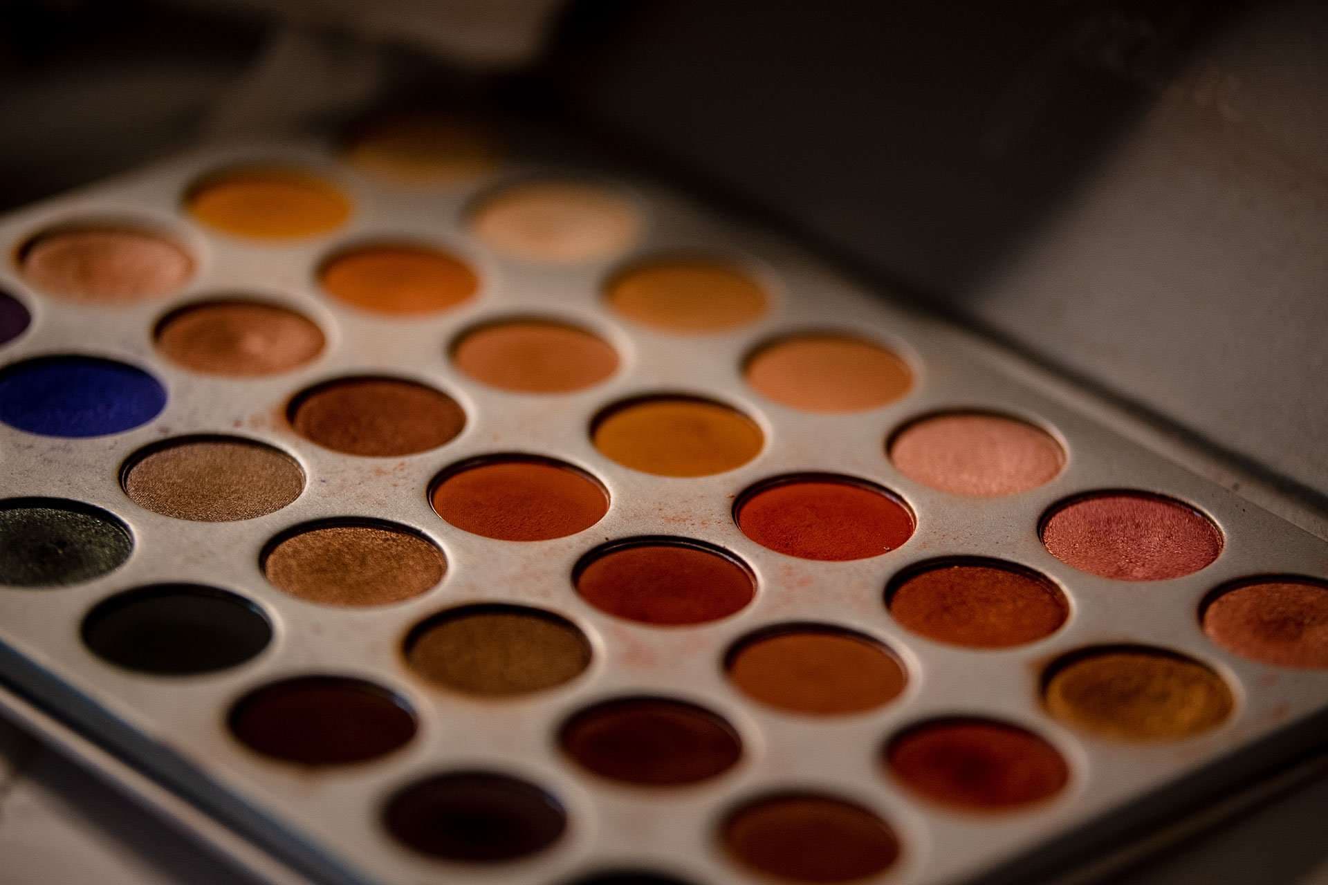 Eyeshadow palette with rows of warm orange, copper, burgundy and brown shades and one blue pan