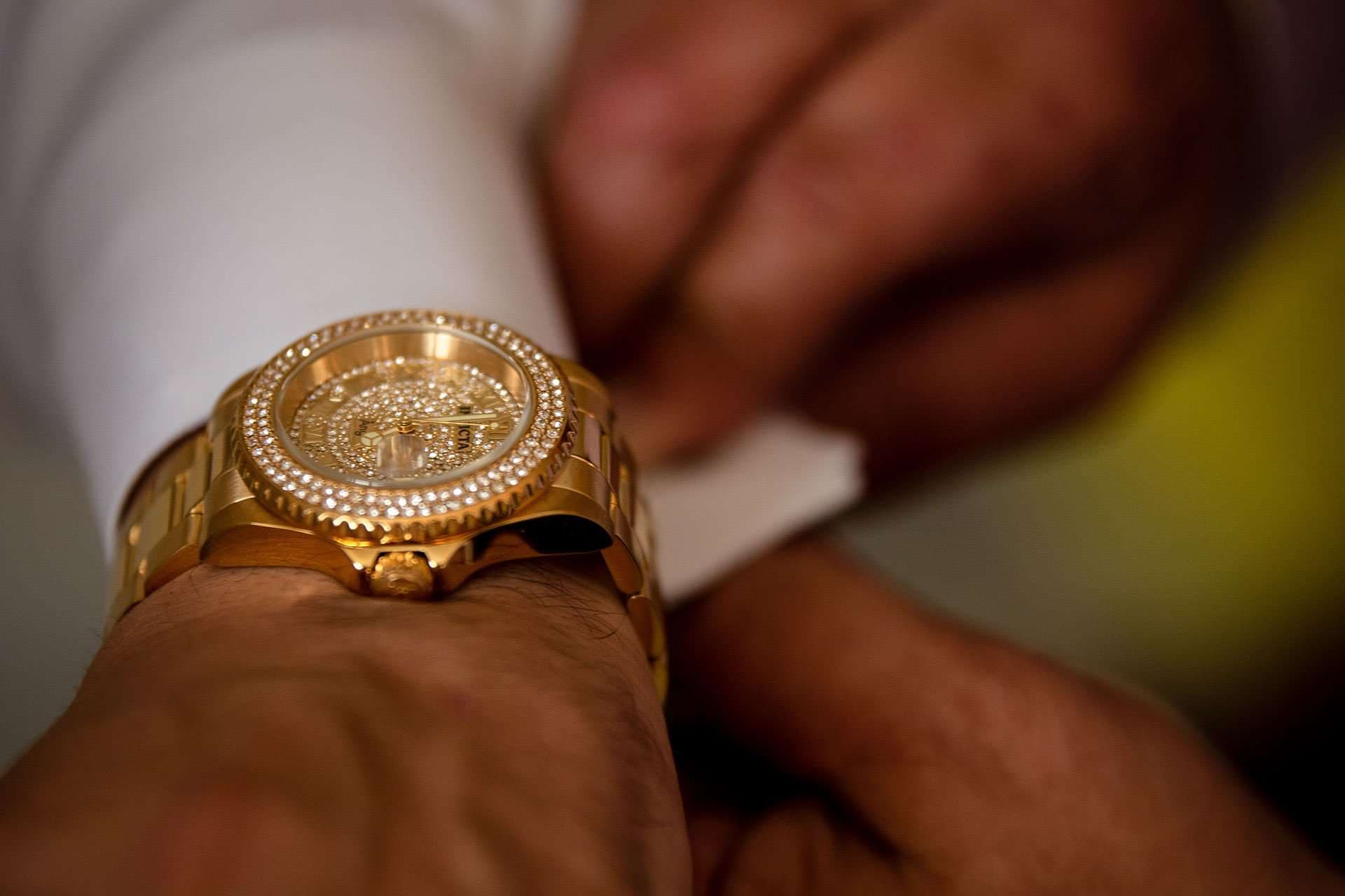 Close-up of a gold diamond-bezel wristwatch on a wrist as he fastens his white shirt cuff