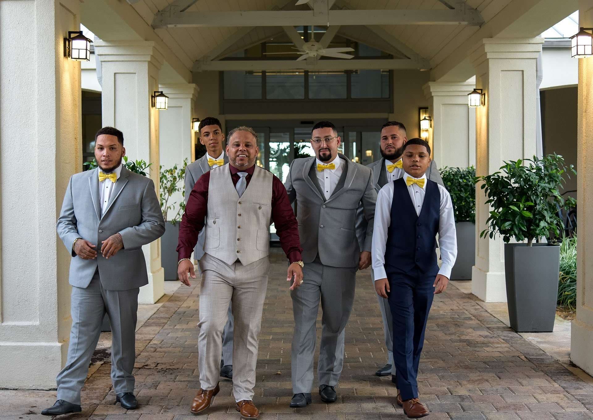 Five men in gray suits and yellow bow ties walking together along a brick covered entrance walkway