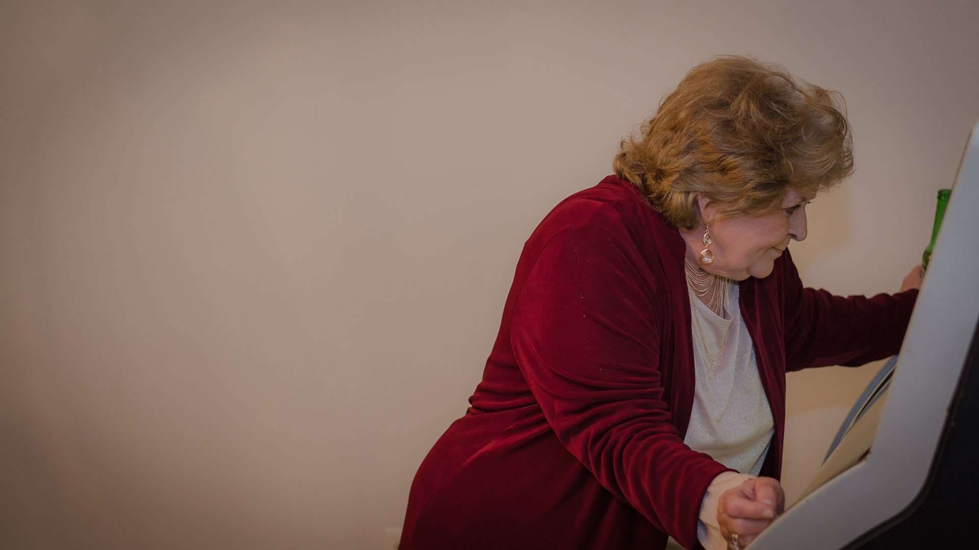 Older wedding guest in a burgundy velvet jacket leaning toward a machine with a clenched fist