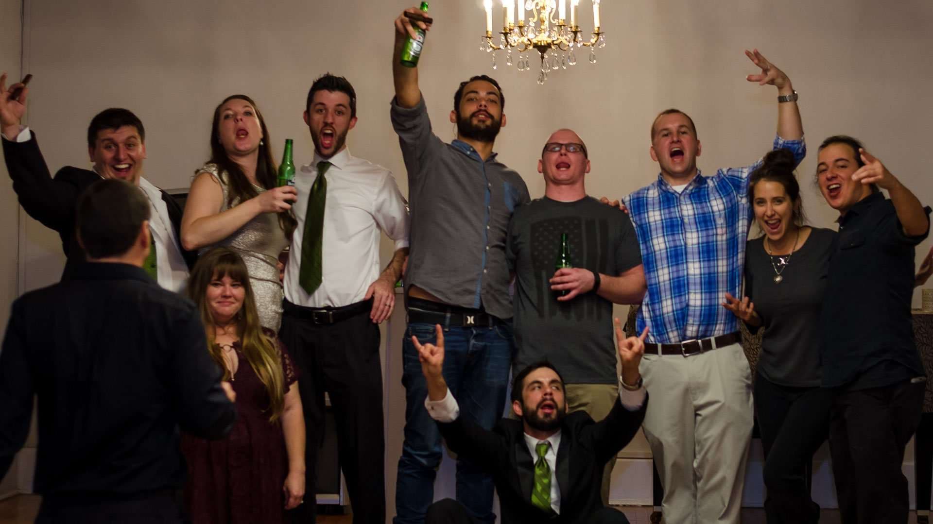 Group of wedding guests cheering and raising beer bottles under a chandelier at the Panama City Women's Club