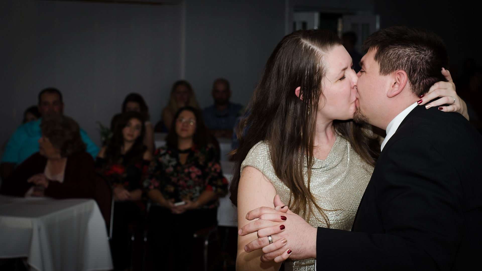 Couple kissing during a first dance while seated wedding guests watch from tables in the background