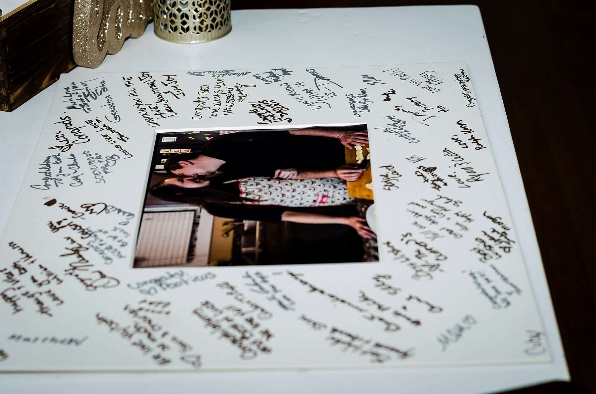 Wedding guest book photo mat covered in handwritten signatures and messages around a framed couple's photo