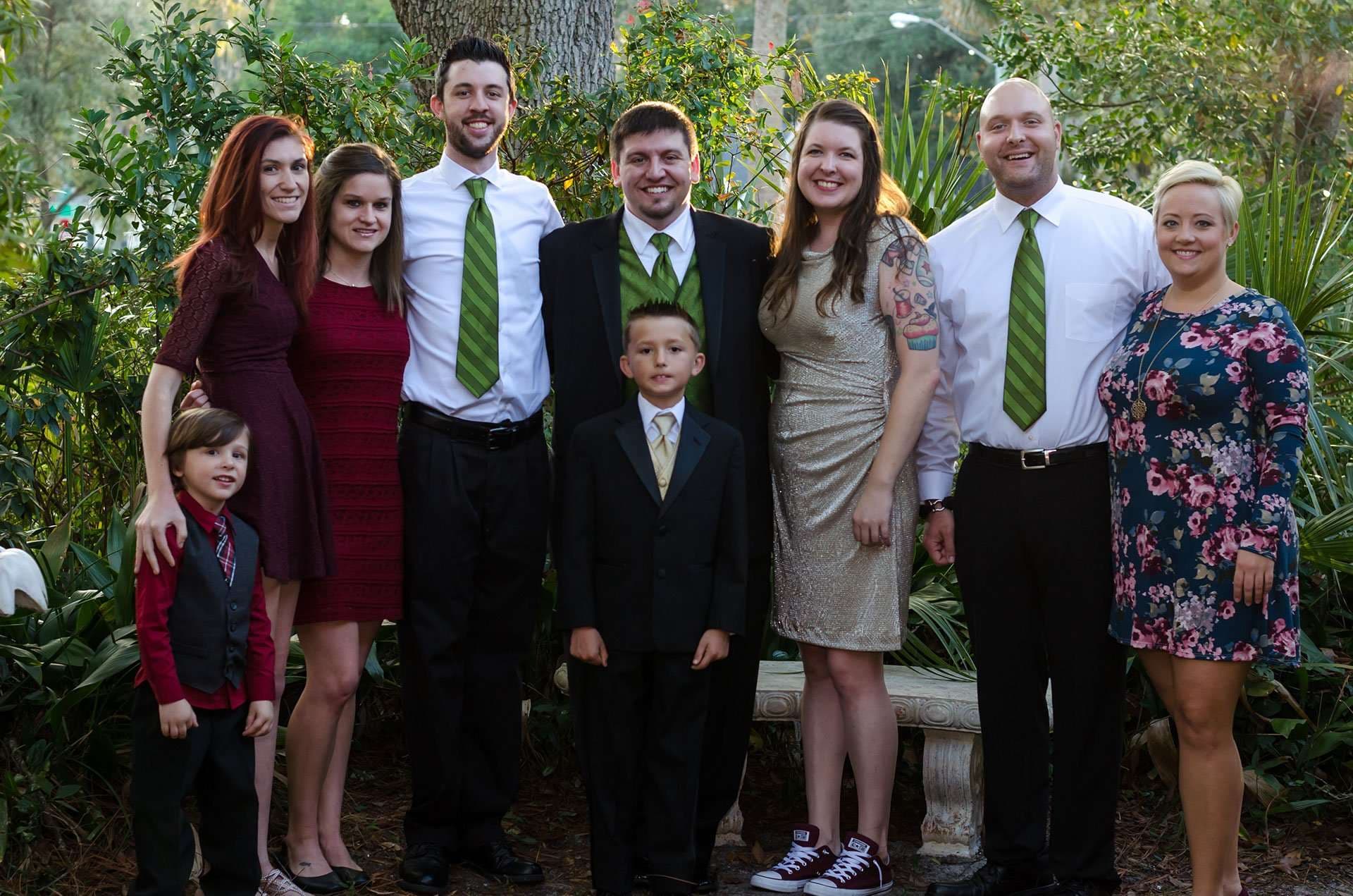 Wedding party and family lined up in front of garden greenery, groomsmen in matching green ties