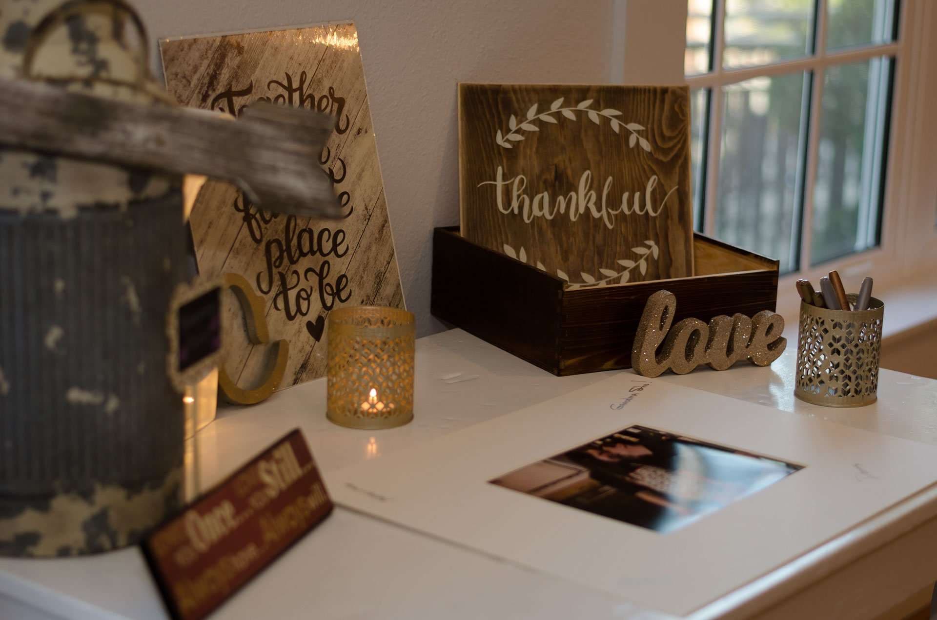 Wedding guest book table with wooden "thankful" sign, "love" letters, candle holder and pen cup beside a matted frame