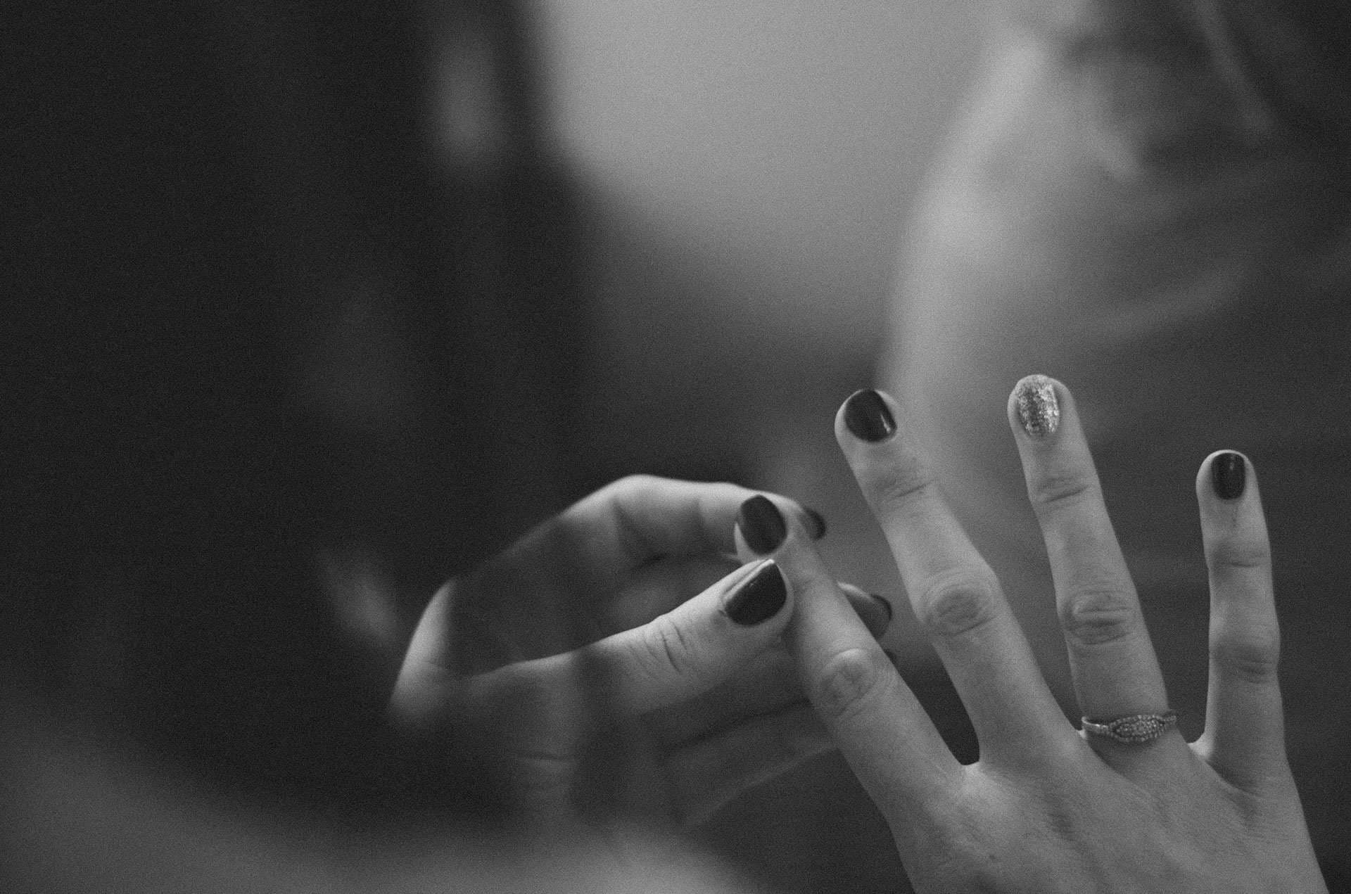 Black-and-white close-up of hands with dark nail polish, one ring finger wearing a silver ring and glittery nail