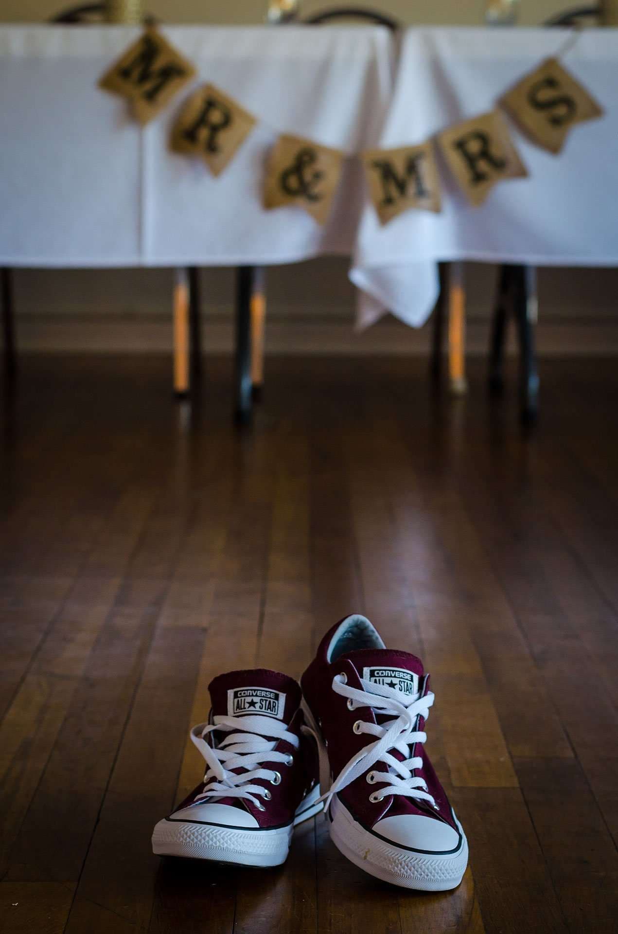 Maroon Converse sneakers on a wood floor in front of a table with a Mr & Mrs burlap banner