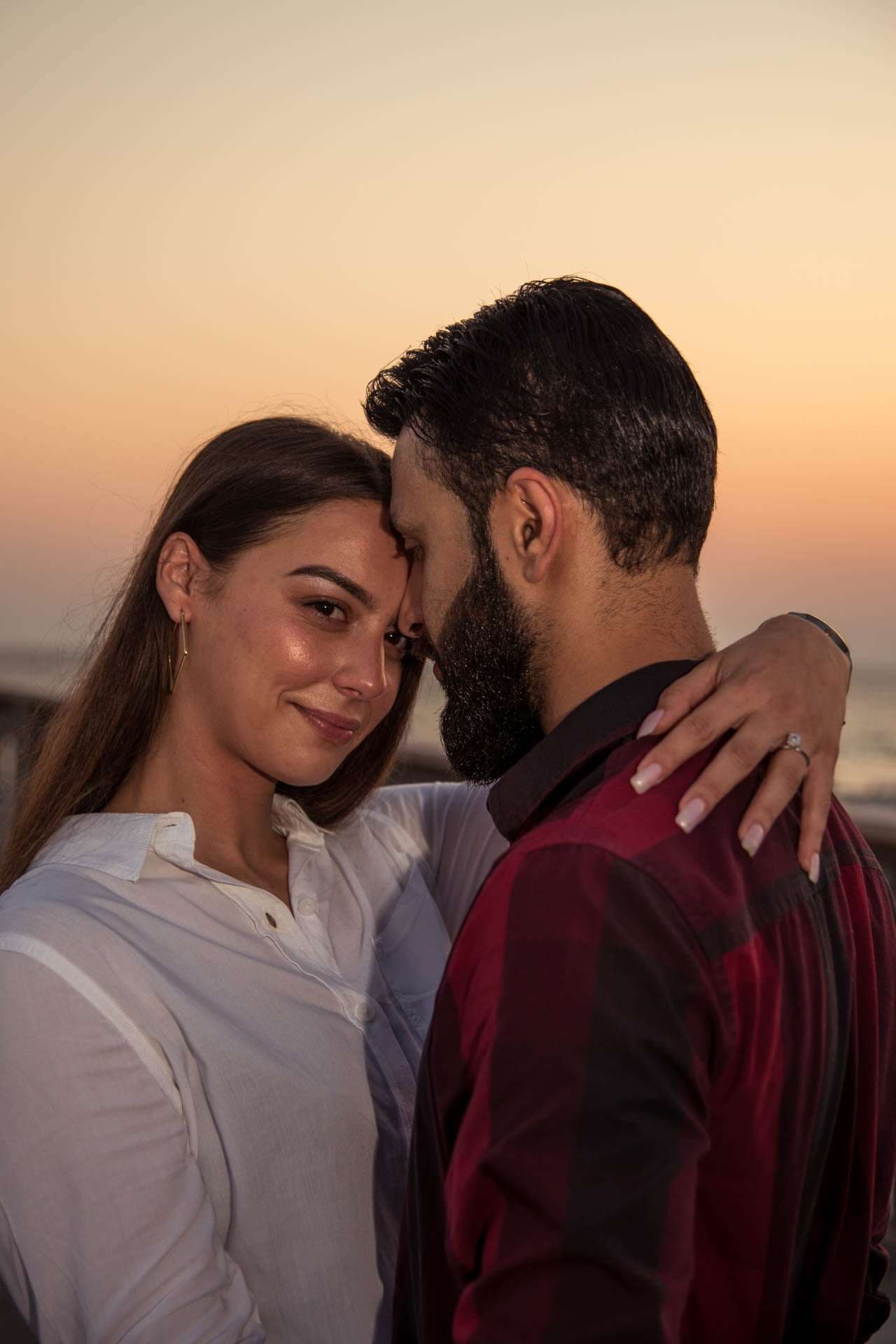 Couple embracing forehead to forehead at sunset on the Panama City Beach City Pier, her ring visible on his shoulder