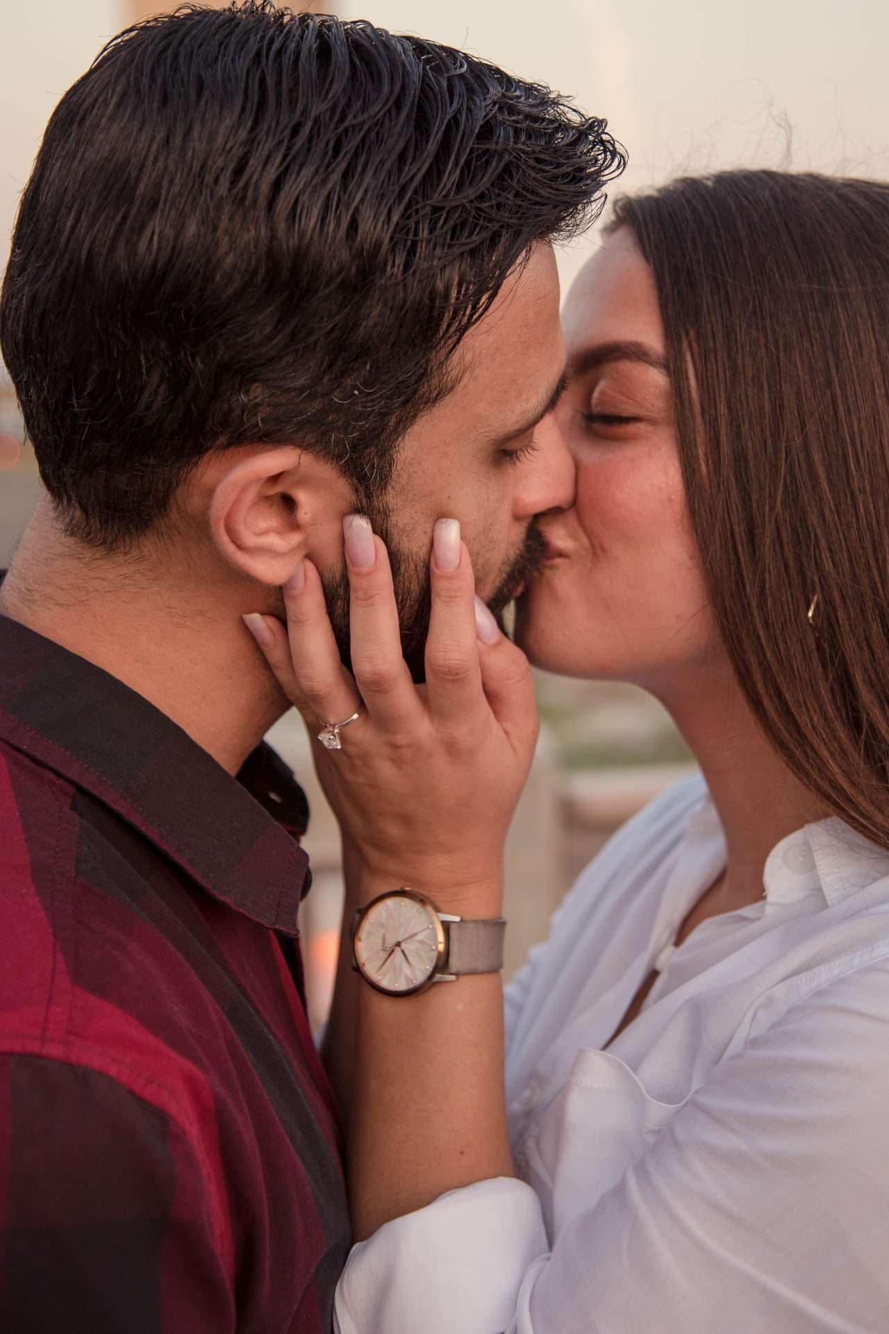 Couple kissing at golden hour as she cups his cheek, engagement ring visible on her hand, at the Panama City Beach pier