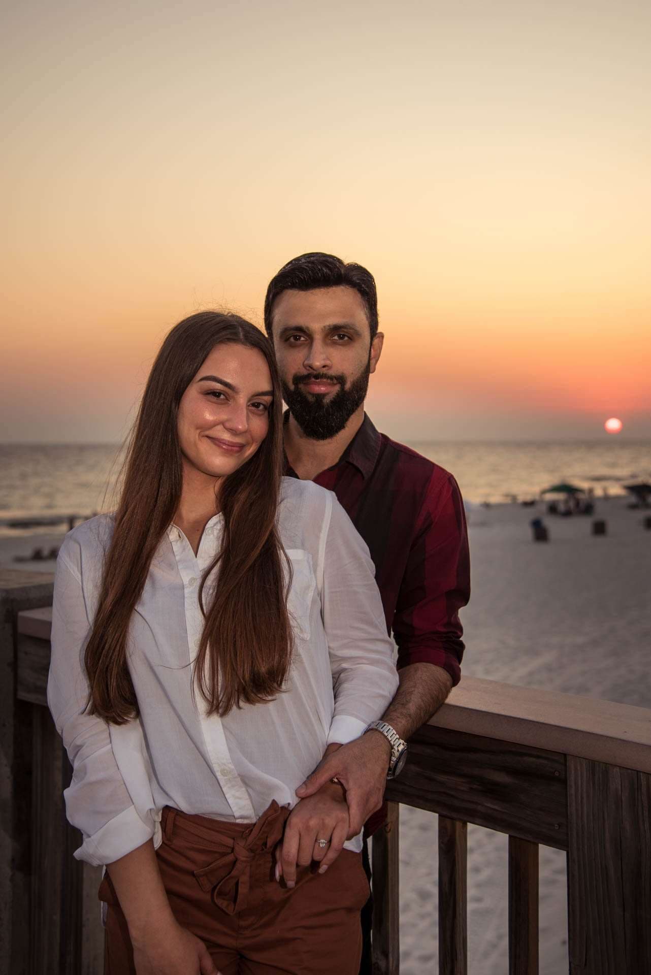 Couple embracing on a wooden railing at the Panama City Beach City Pier as the sun sets over the water