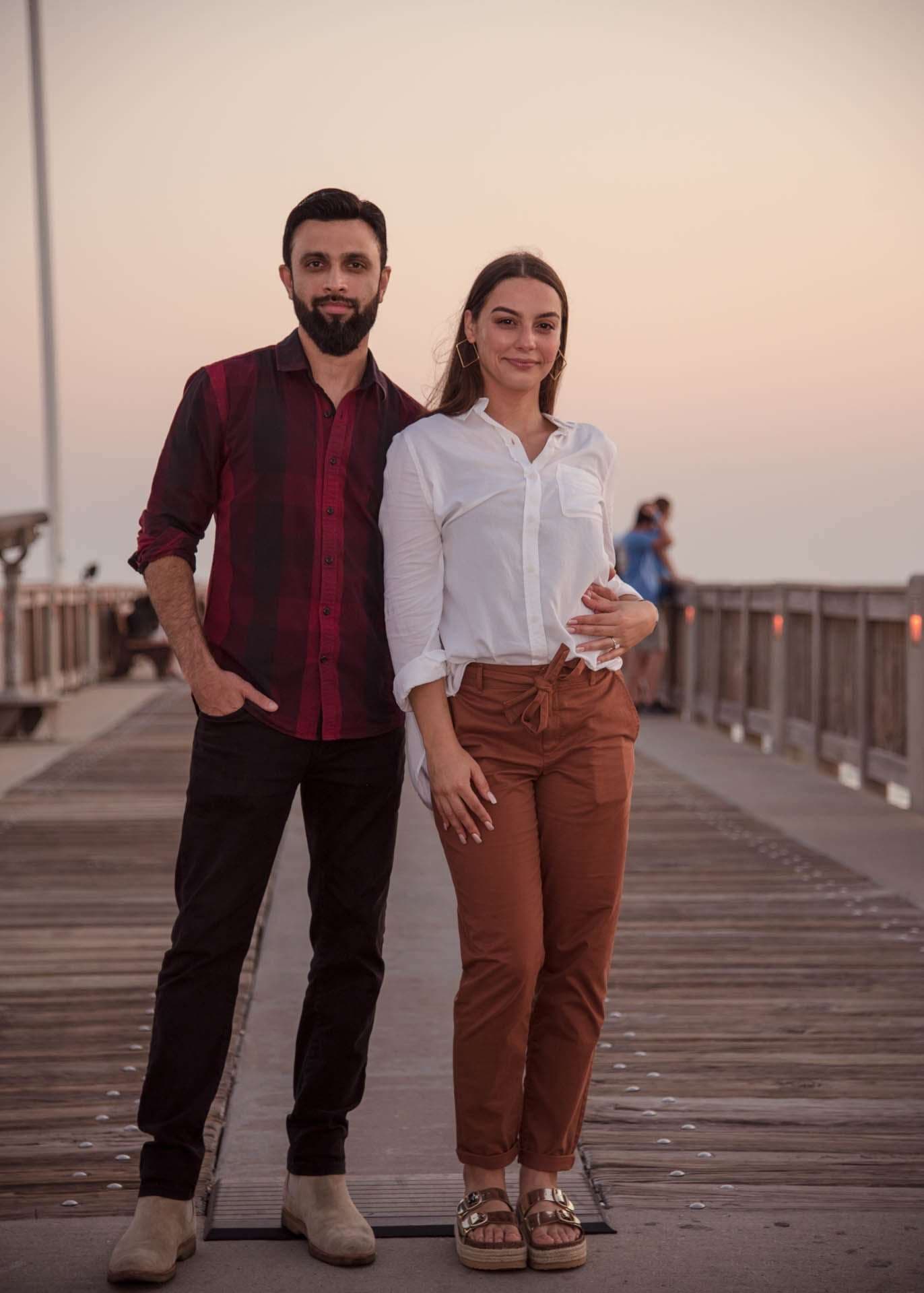 Couple standing close on the Panama City Beach City Pier at dusk, she wears a white blouse and he a plaid shirt