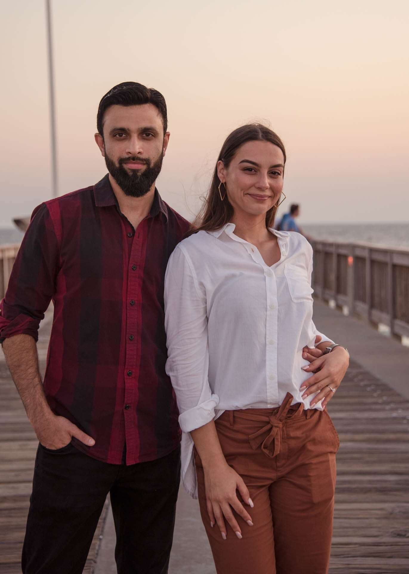 Couple posing close together on the Panama City Beach City Pier at sunset, he in a plaid shirt, she in white