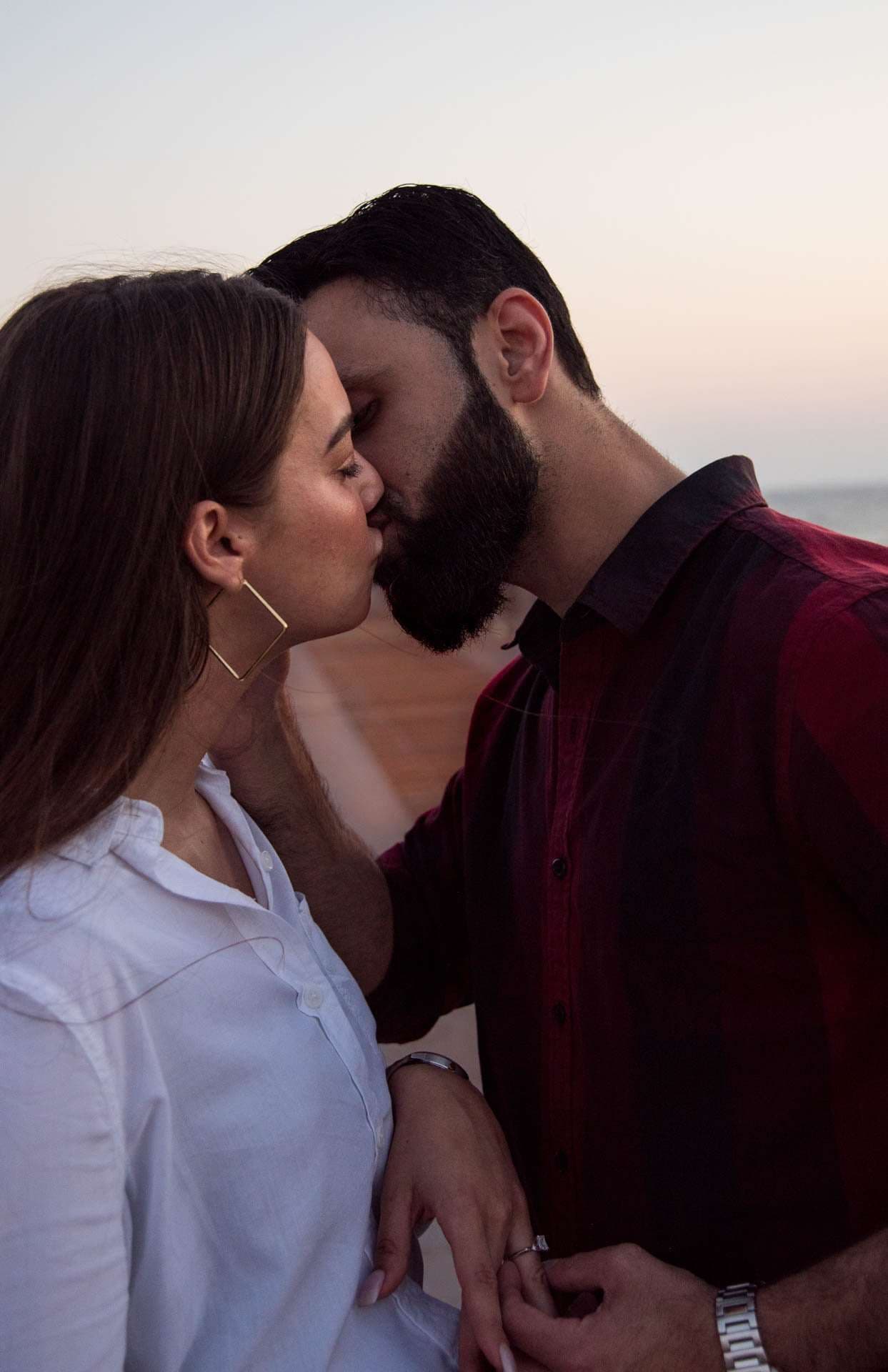 Couple kissing at dusk on the Panama City Beach City Pier, her hand with a ring resting on his arm