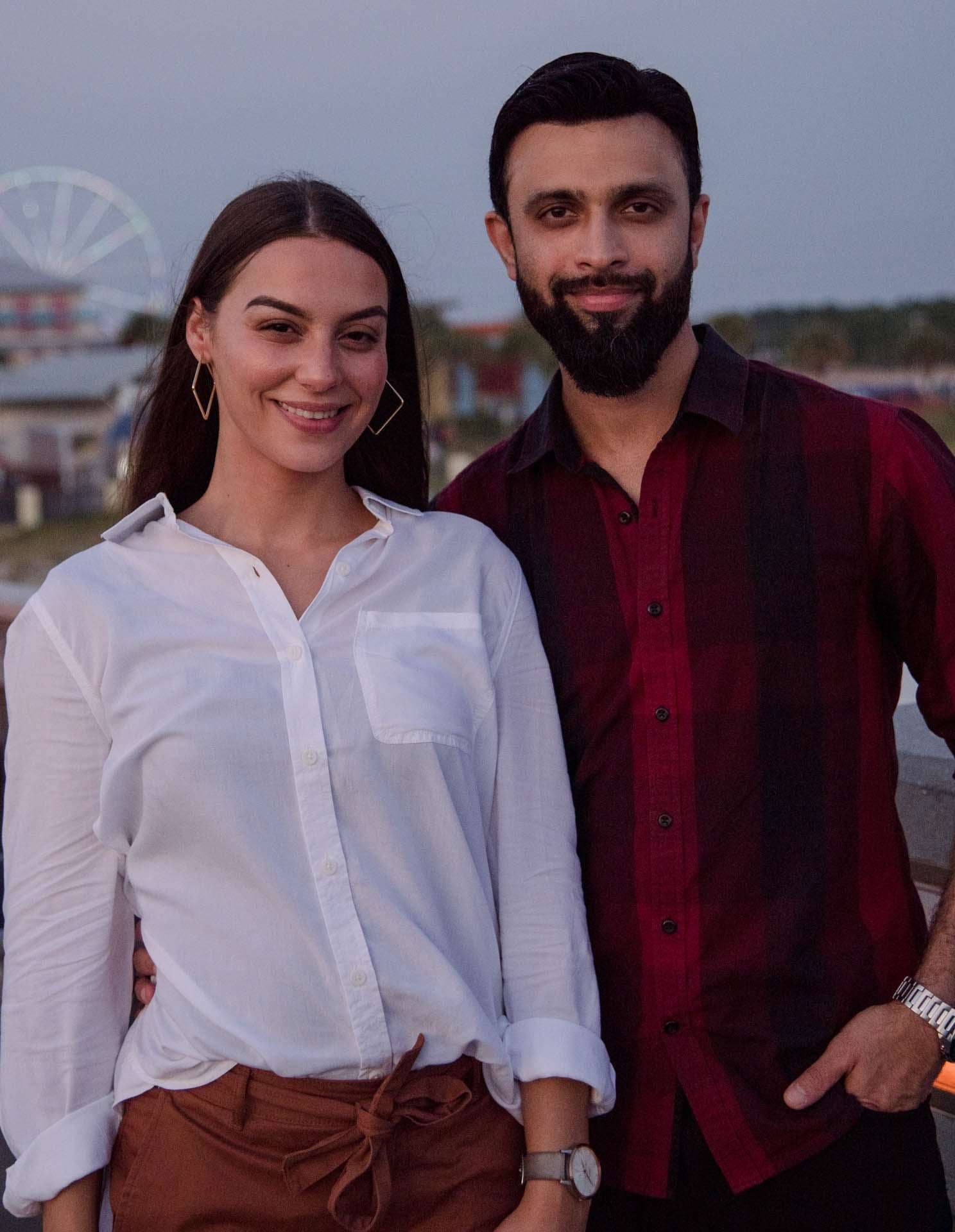 Smiling couple posing close together on the Panama City Beach City Pier at dusk, with a Ferris wheel behind them