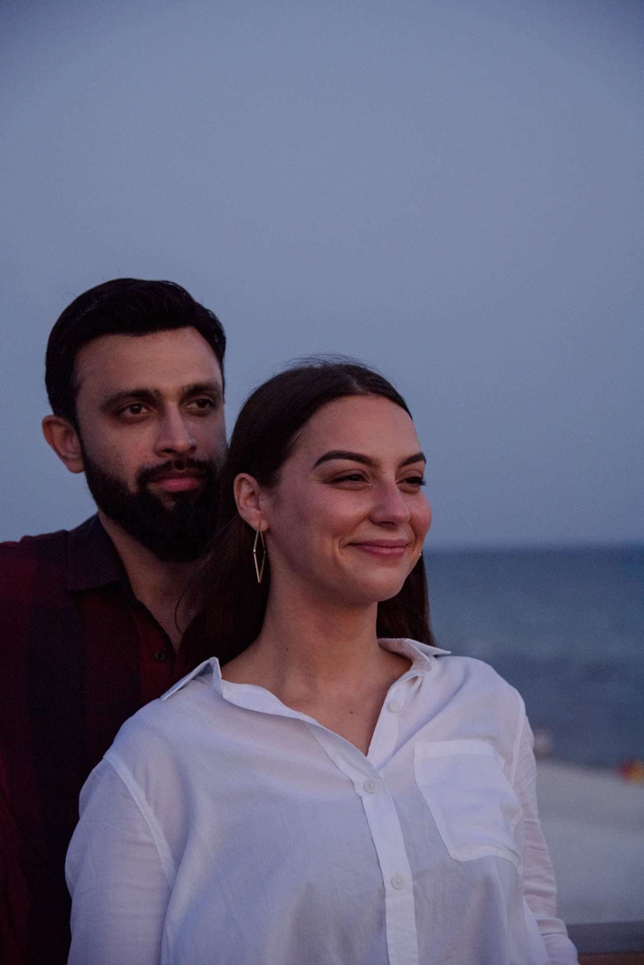 Smiling woman in a white shirt with a bearded man standing behind her at the Panama City Beach City Pier at dusk