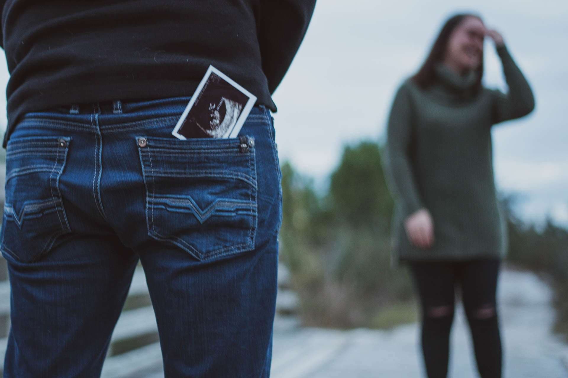 Ultrasound photo tucked in a man's back jeans pocket while a woman stands blurred behind him at Camp Helen State Park