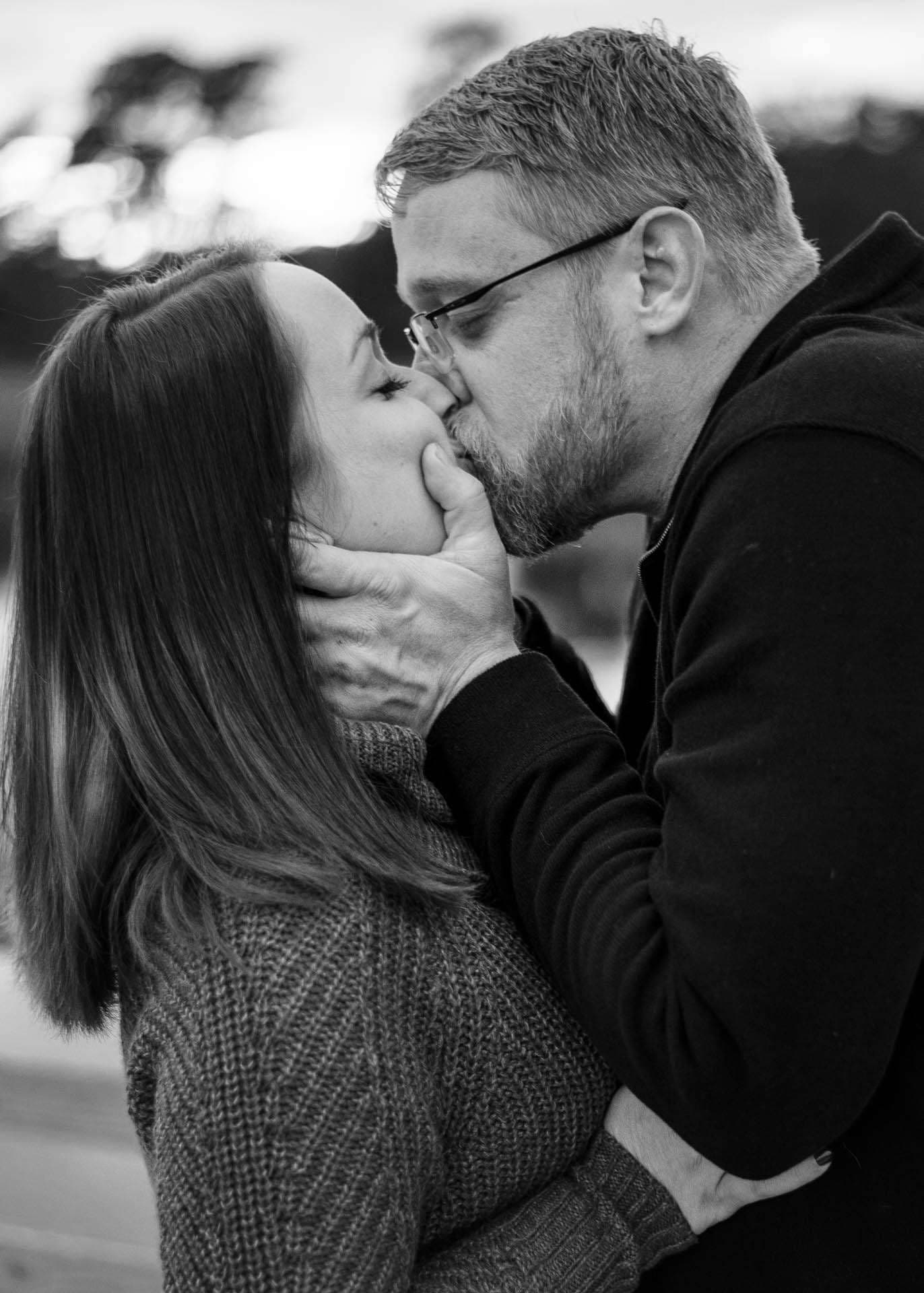 Black-and-white close-up of a couple kissing at Camp Helen State Park, his hand cradling her face