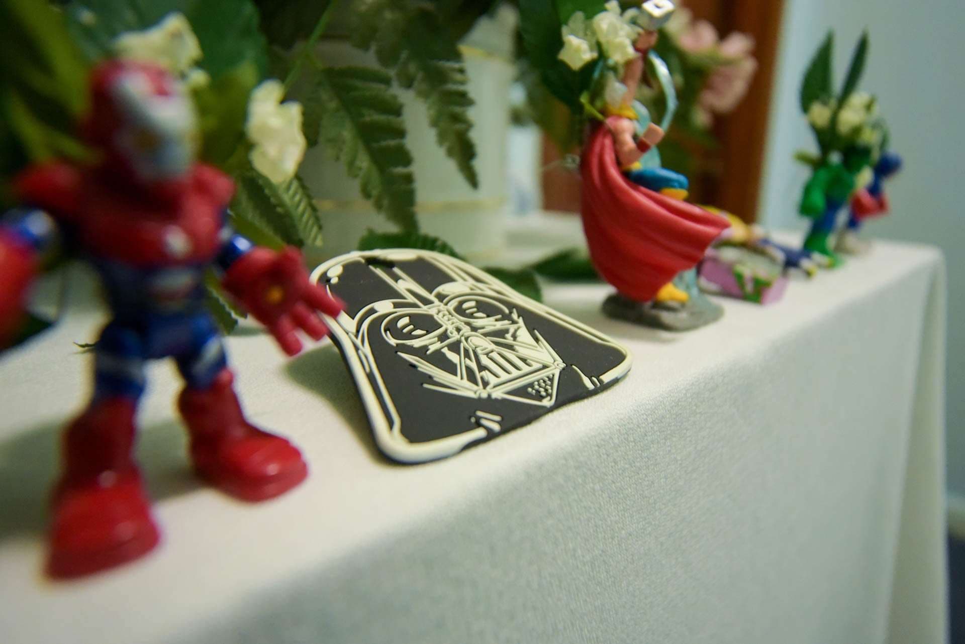 Darth Vader patch and superhero toy figures on a white tablecloth among flowers and ferns at a wedding