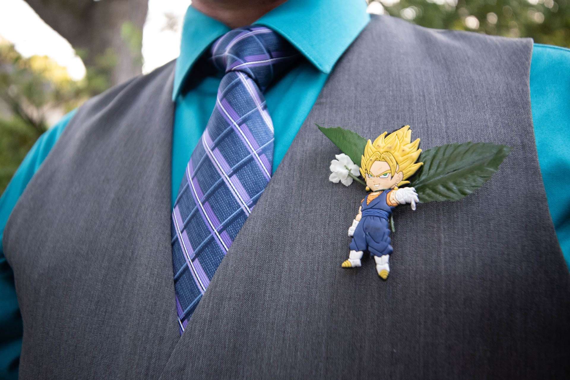 Dragon Ball character boutonniere with leaves pinned to a gray vest, teal shirt and purple plaid tie