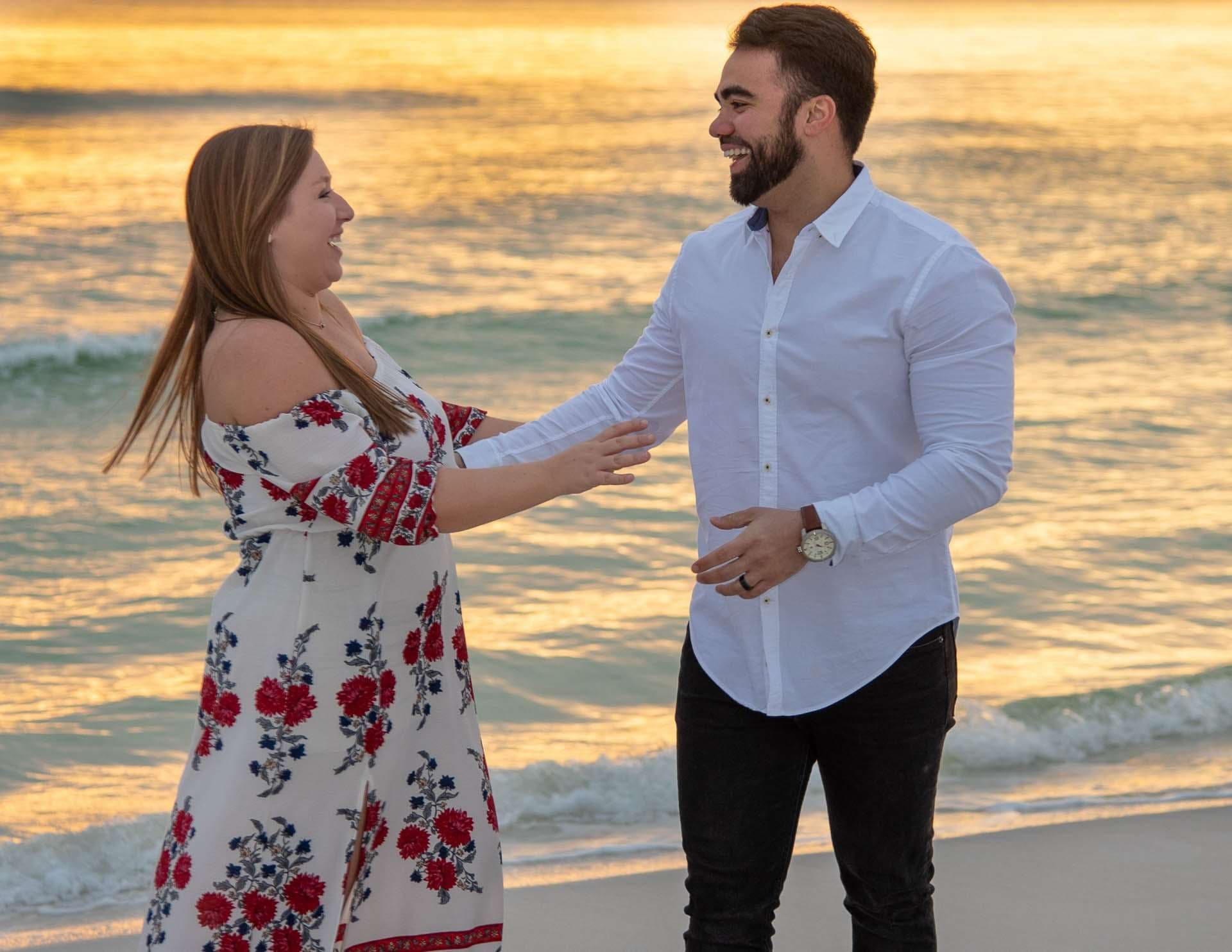 Couple laughing and reaching for each other's hands on the beach at Grayton Beach during a golden sunset