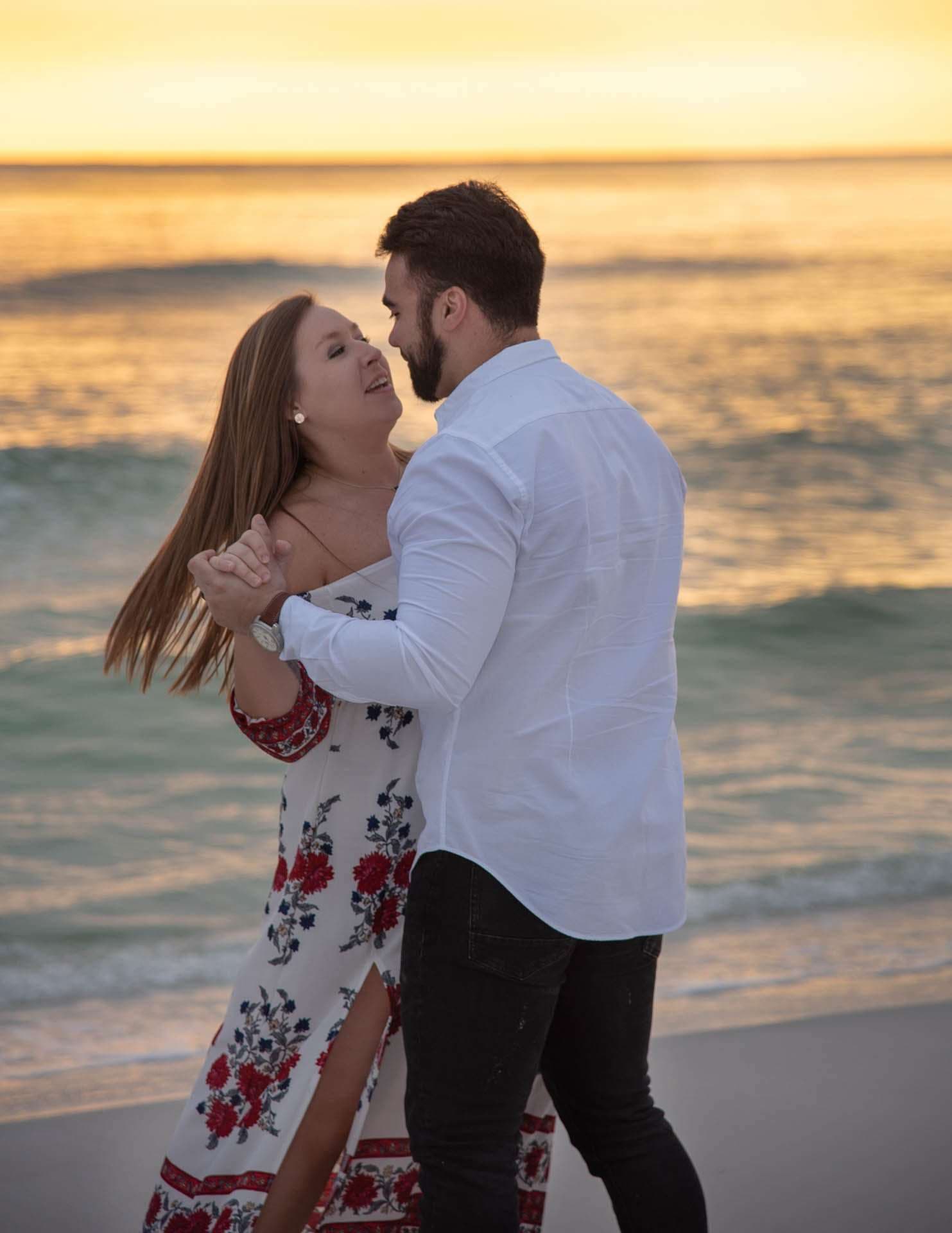 Couple dancing close on Grayton Beach at sunset, she wears a floral maxi dress and he a white shirt