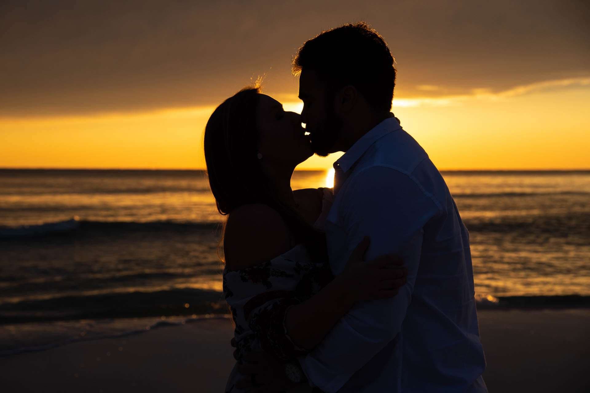 Silhouetted couple kissing on the beach at Grayton Beach as the sun sets over the water