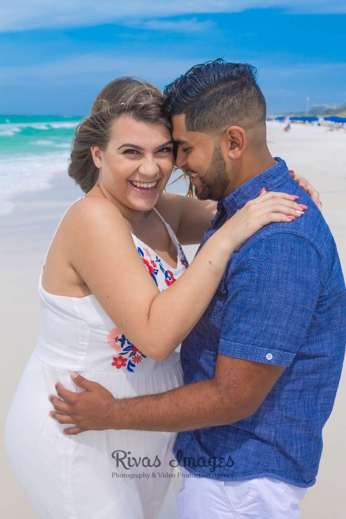Smiling couple embracing forehead to forehead on a sunny beach in Seaside, Florida, woman in white embroidered dress