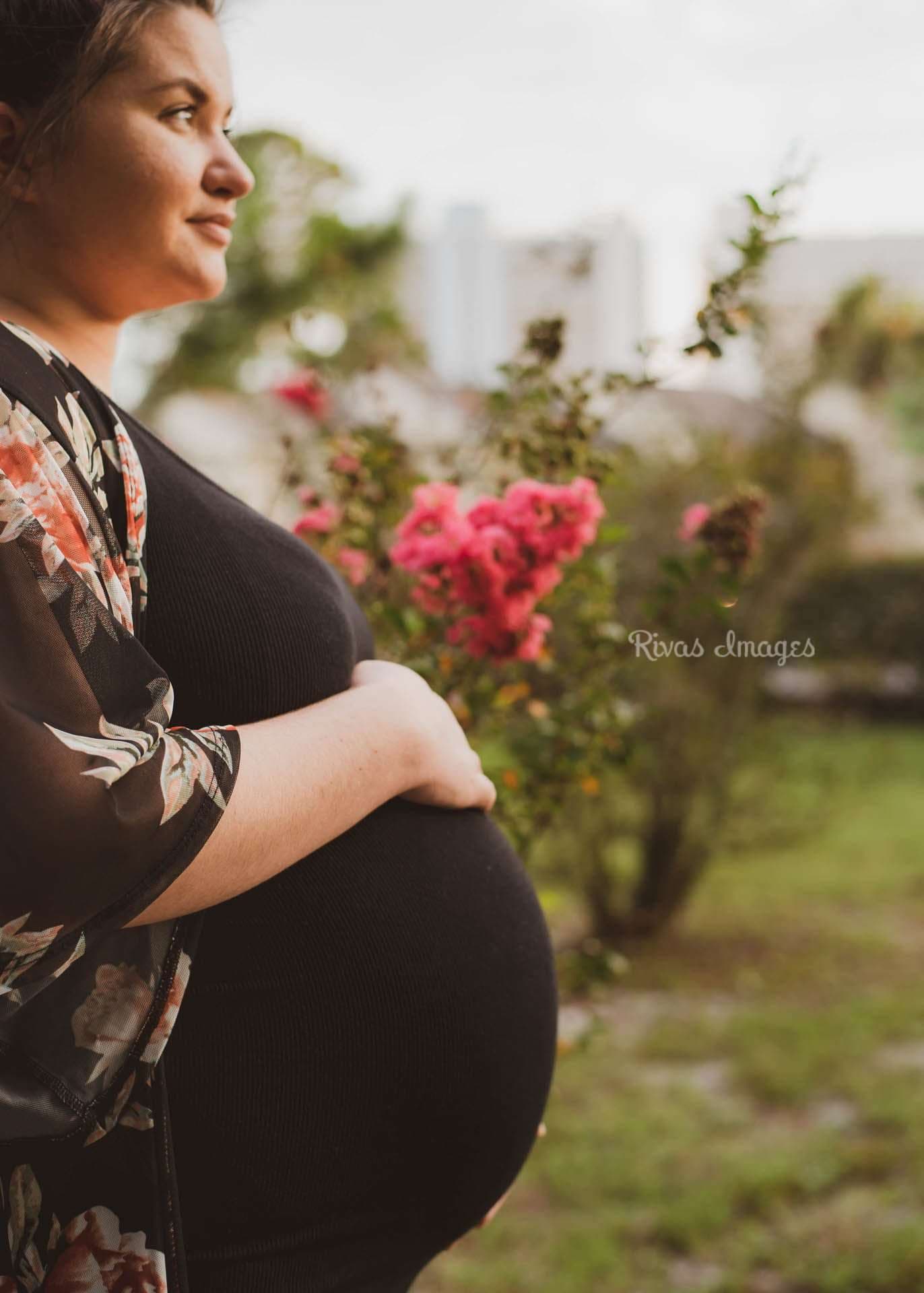 Expecting mother in a floral kimono cradling her belly beside a pink flowering bush