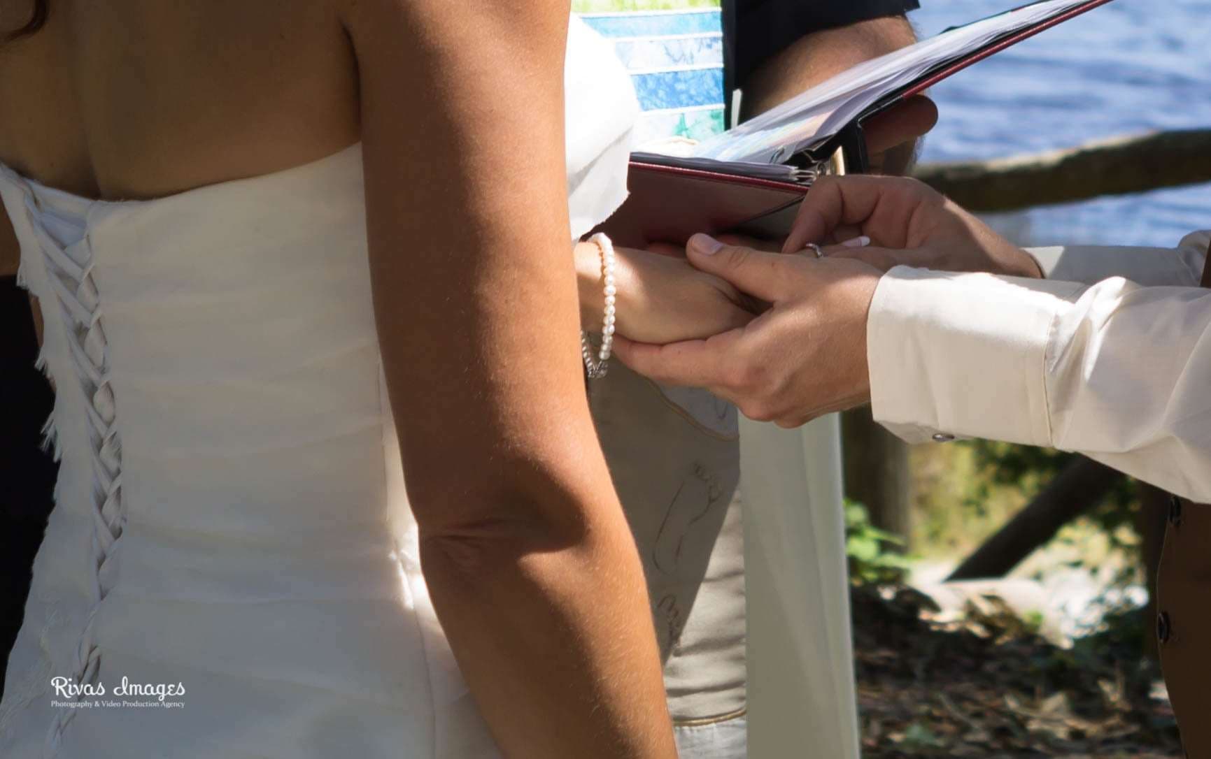 Hands joining during a wedding ceremony by the water at Camp Helen State Park, bride in a white corset-back gown