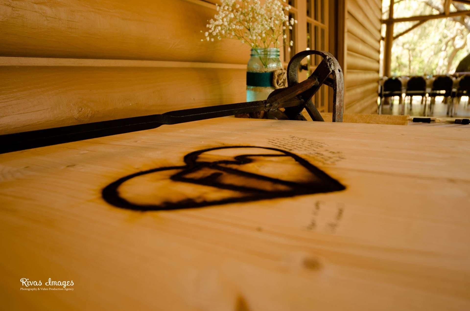 Heart branded into a wooden guest book board with an iron branding tool, baby's breath in a jar behind it