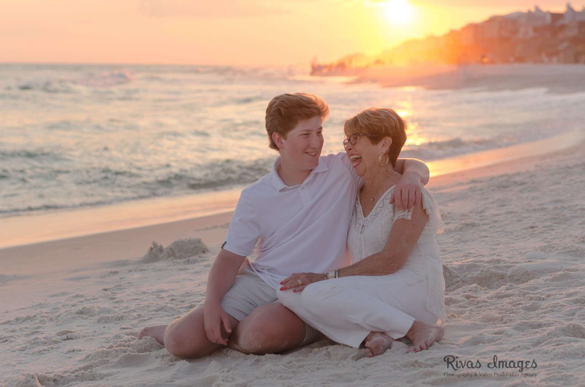 Teen boy and older woman laughing together on the sand at Rosemary Beach at sunset, both in white