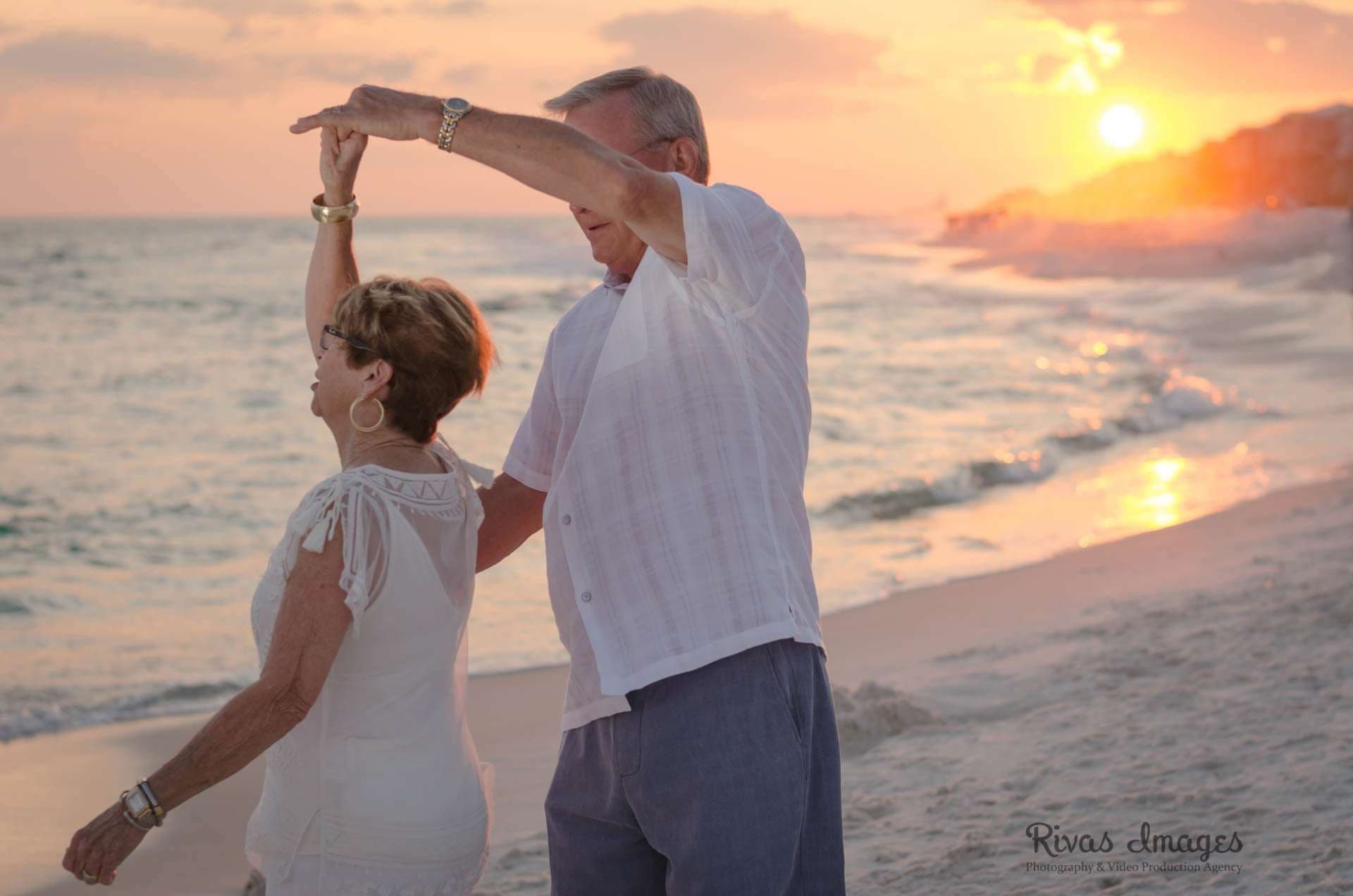 Older couple dancing on the beach at sunset, the man twirling the woman in a white top