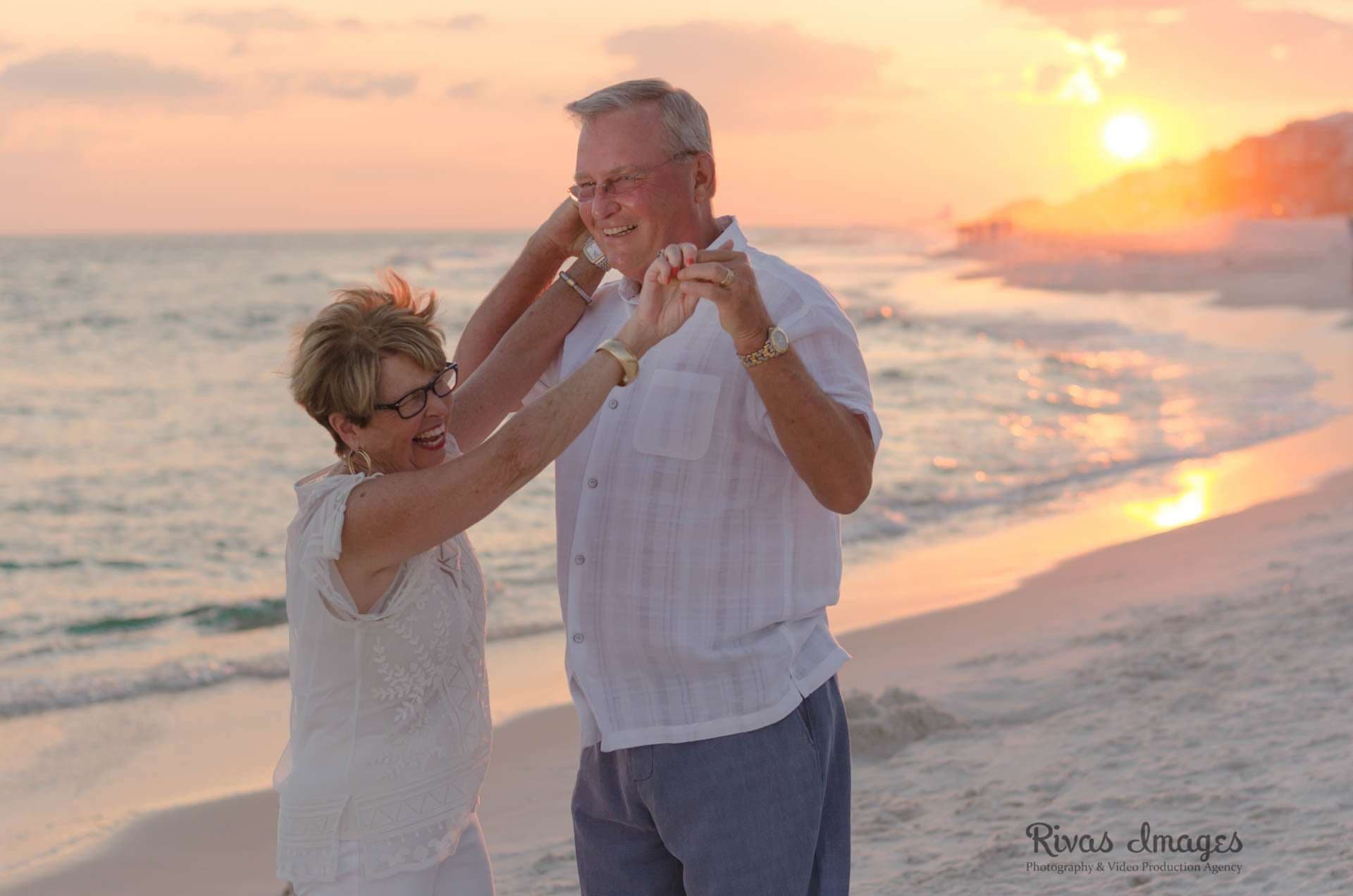 Older couple dancing hand in hand on the beach at Rosemary Beach as the sun sets over the water