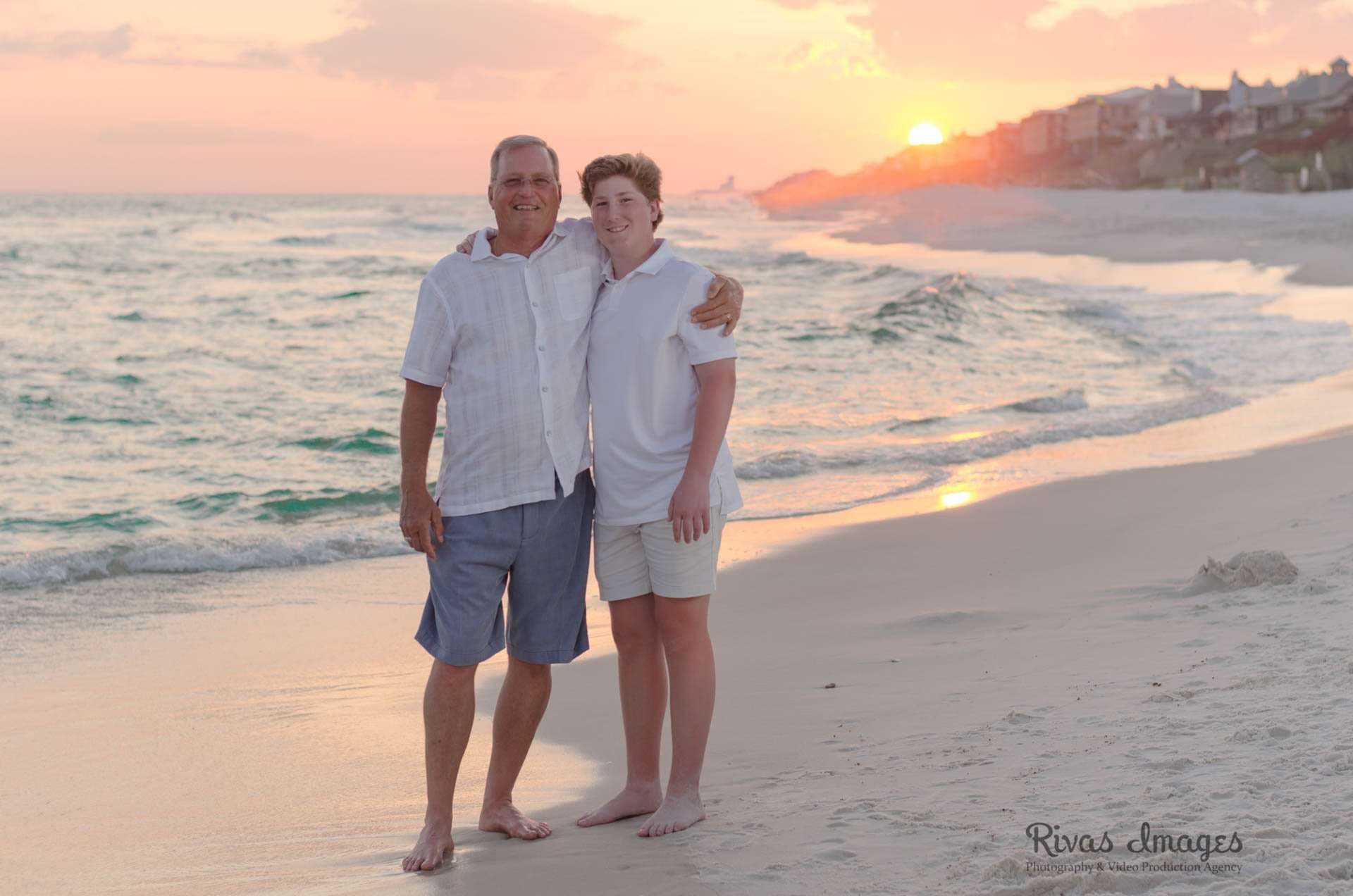 Older man and teenage boy in white shirts embracing barefoot on the beach at Rosemary Beach as the sun sets