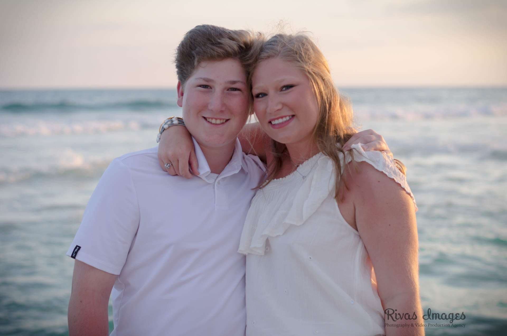 Smiling teen in a white polo and woman in a white ruffled top embracing on the beach at sunset in Rosemary Beach