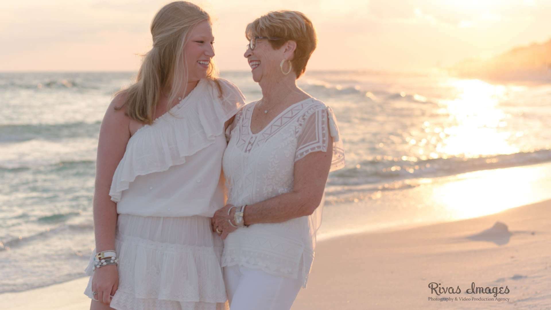Two smiling women in white embracing and laughing together on the beach at sunset in Rosemary Beach