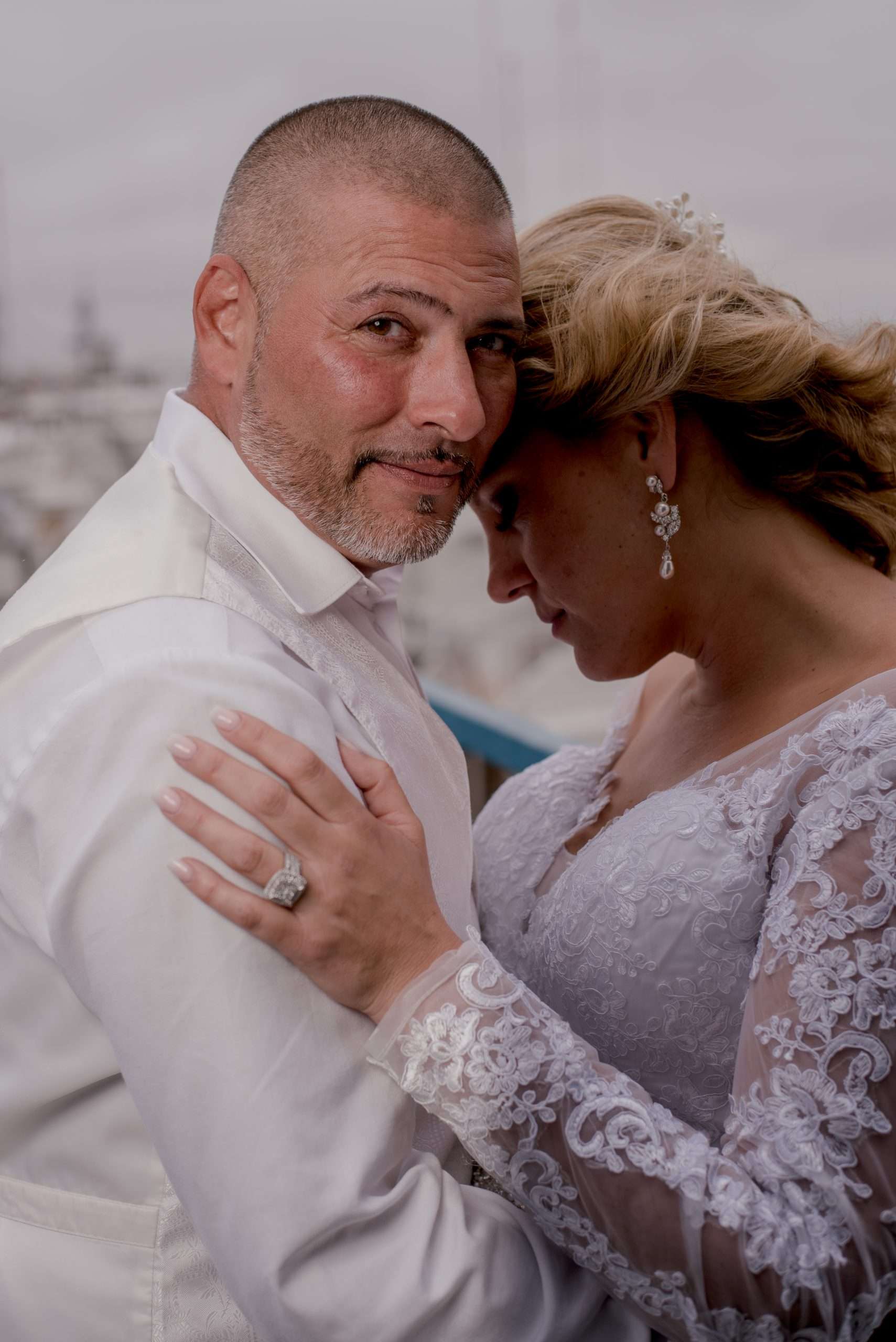 Groom in white shirt and vest embracing his bride in a lace gown, her forehead resting against his cheek
