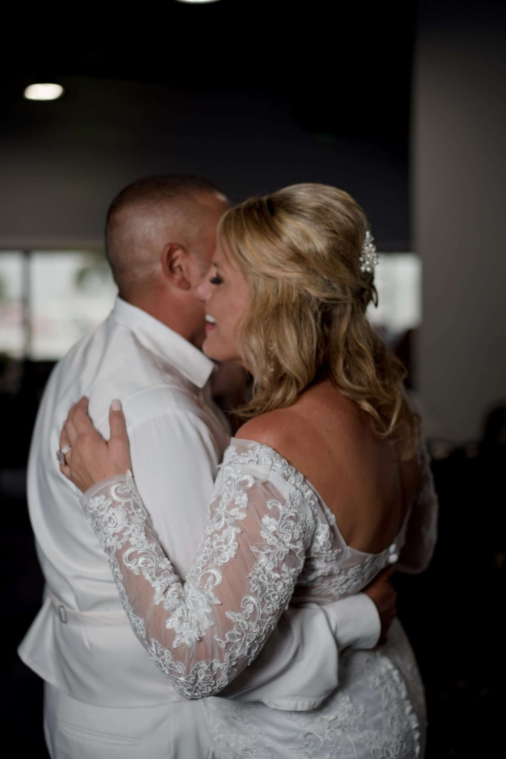 Couple embracing in a slow dance, bride in a white lace off-the-shoulder gown smiling against her partner's cheek