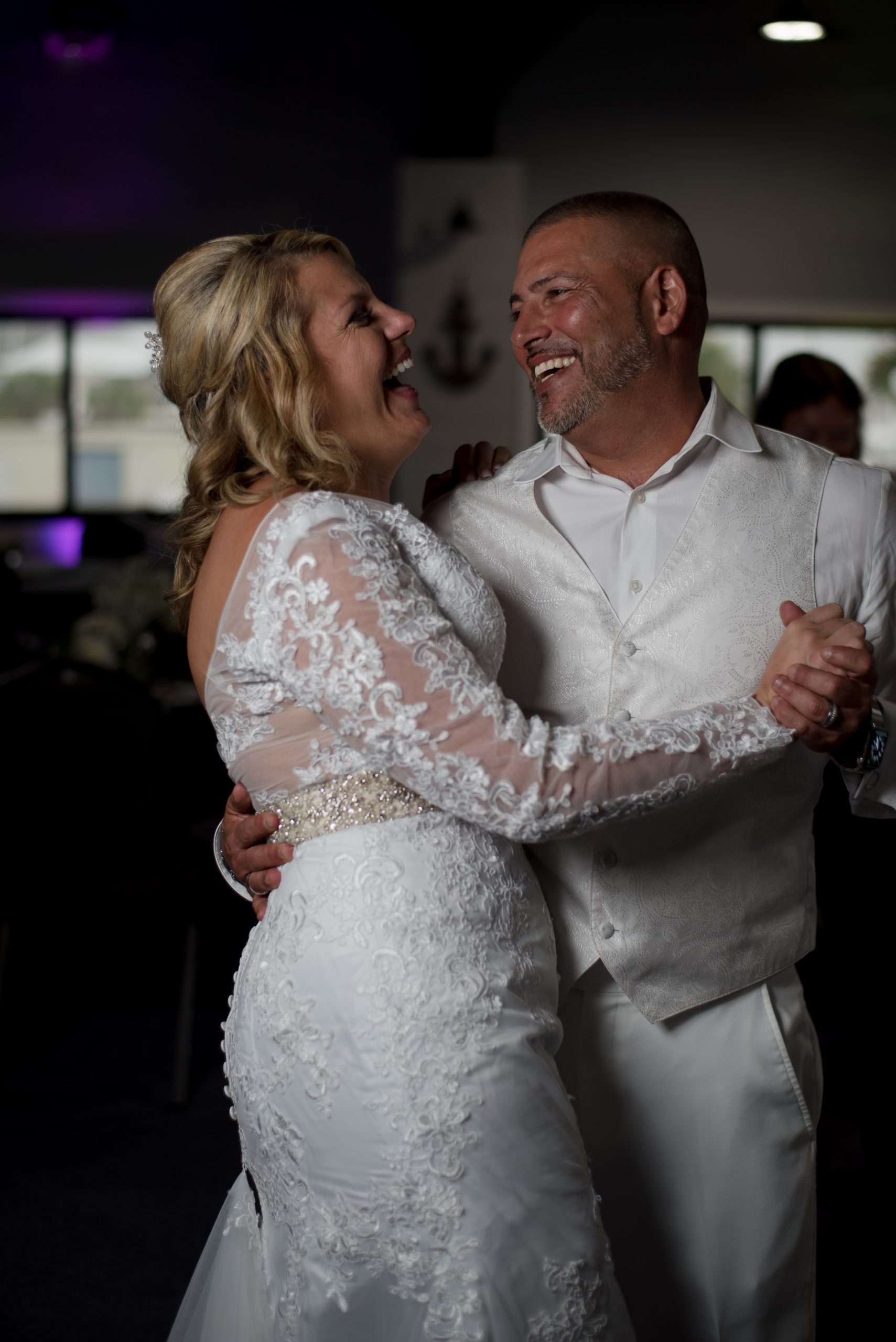 Couple laughing while dancing, the bride in a long-sleeved white lace gown and the groom in a white vest