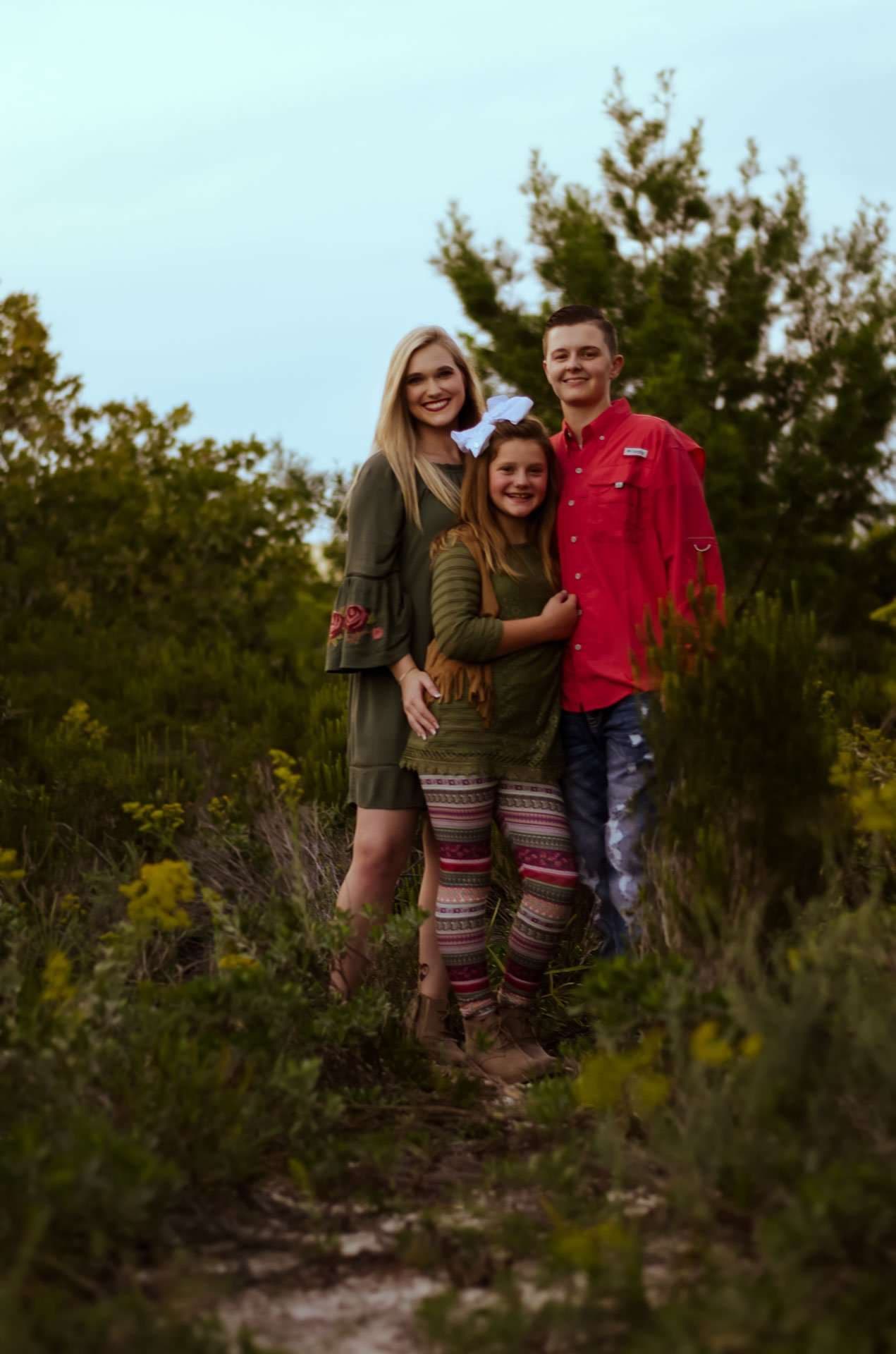 Young woman, girl with a big bow and teenage boy in red shirt posing together on a wooded trail